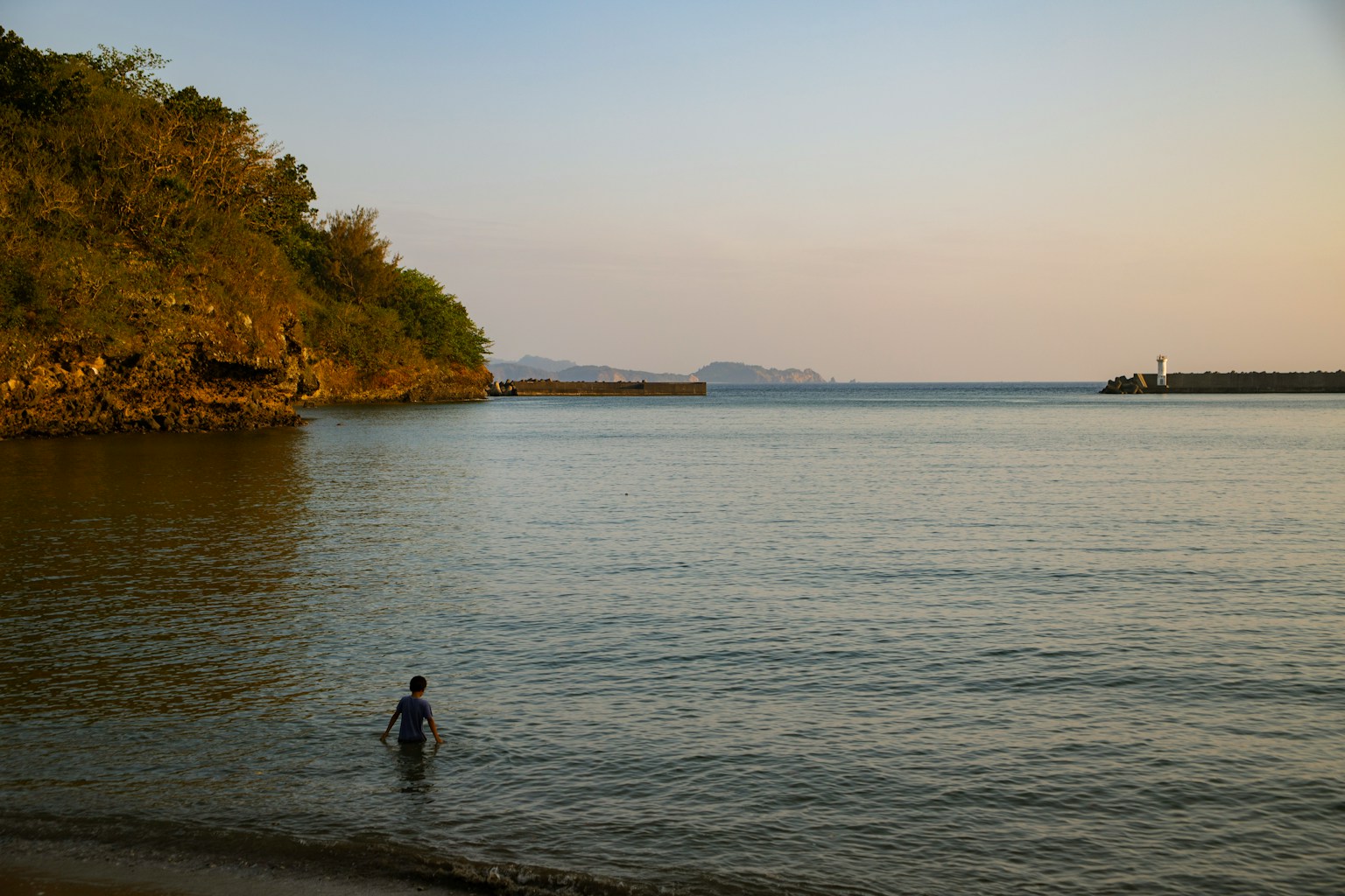穏やかな海に立つ人物と静かな夕暮れの風景