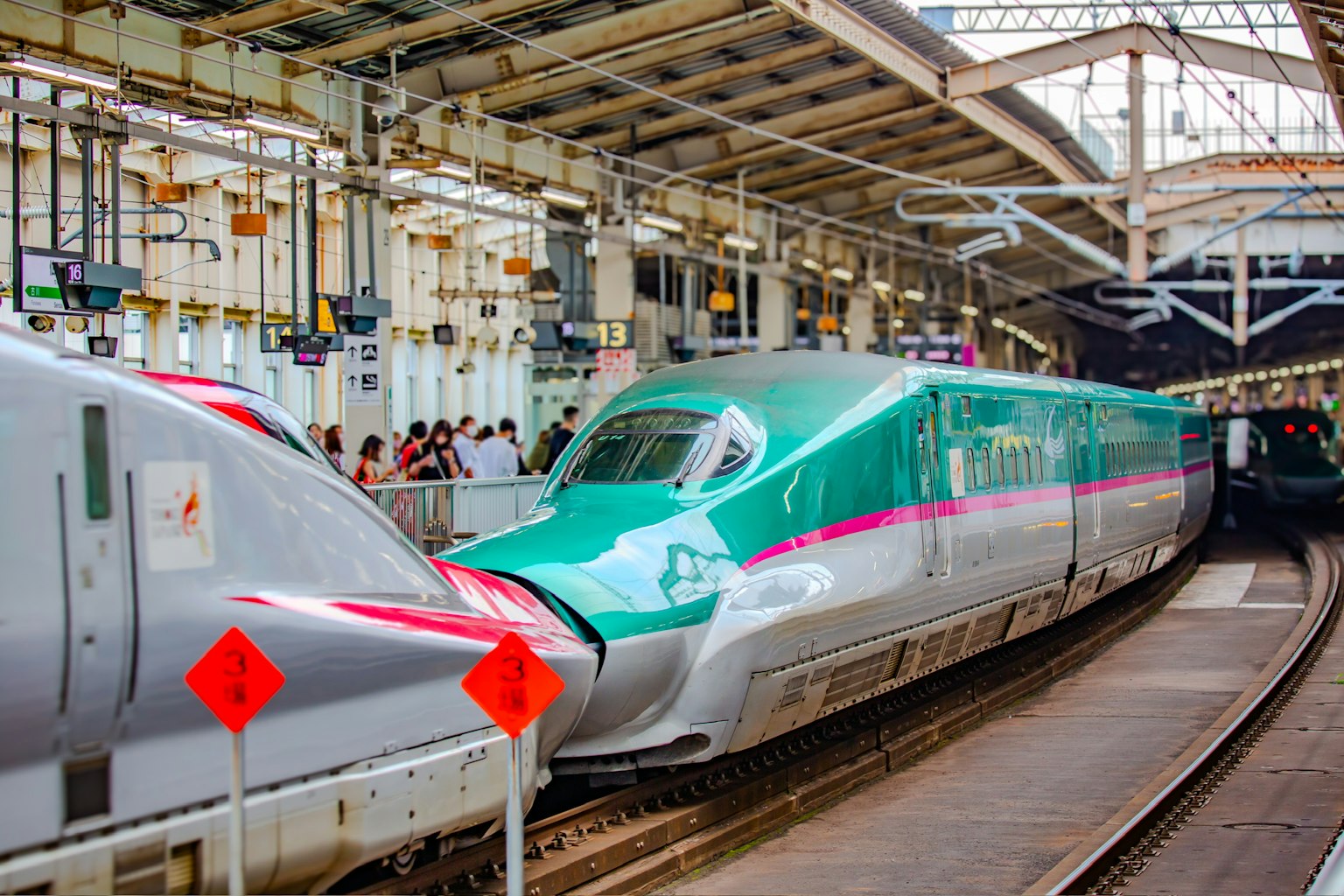 Shinkansen hijau dan putih di stasiun dengan orang-orang di sekitarnya