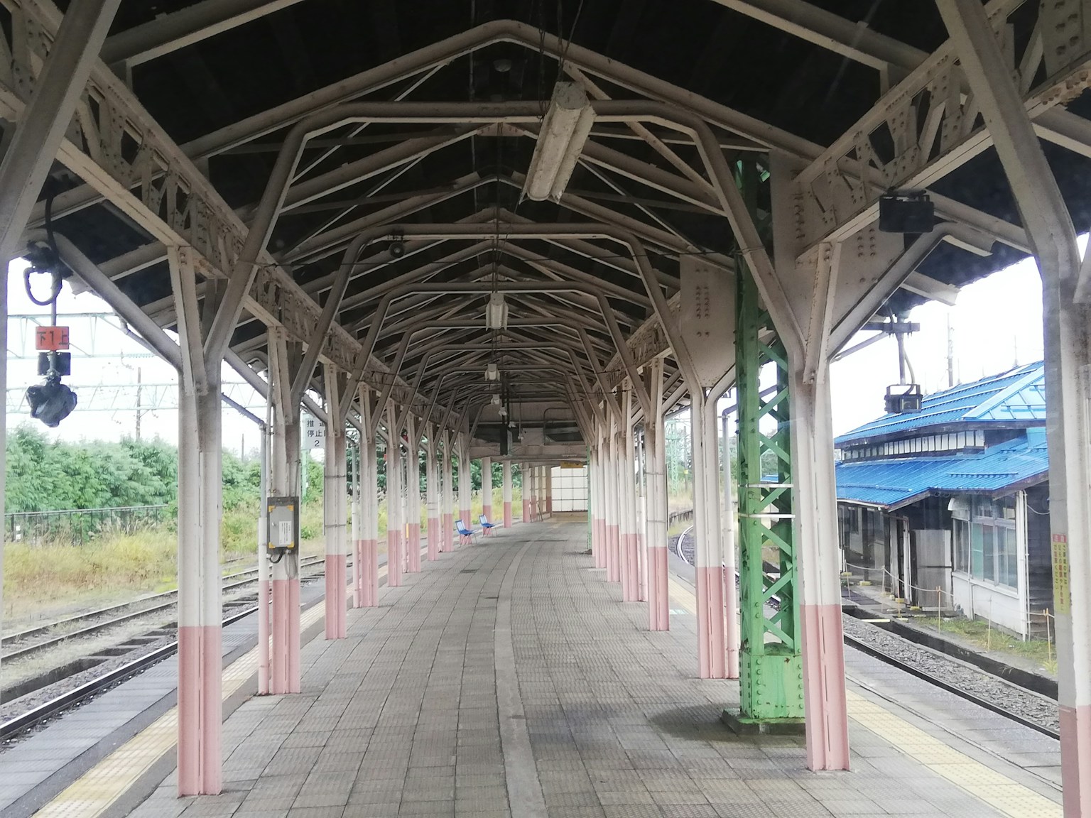 Platform stasiun kereta tua dengan struktur kayu dan bangunan atap biru