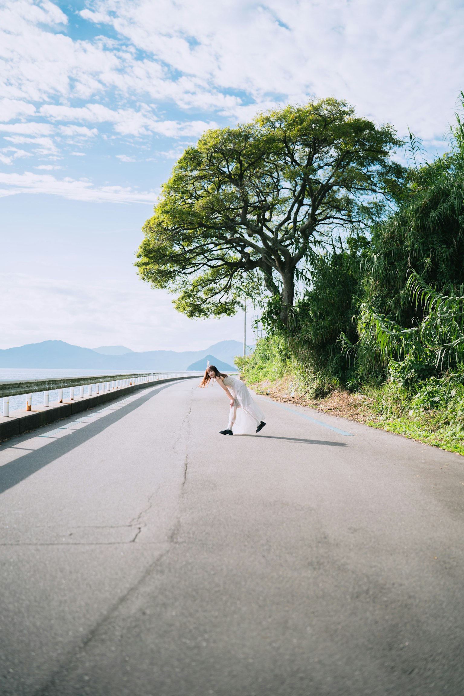 在綠色樹木和藍天下蹲在道路上的女性