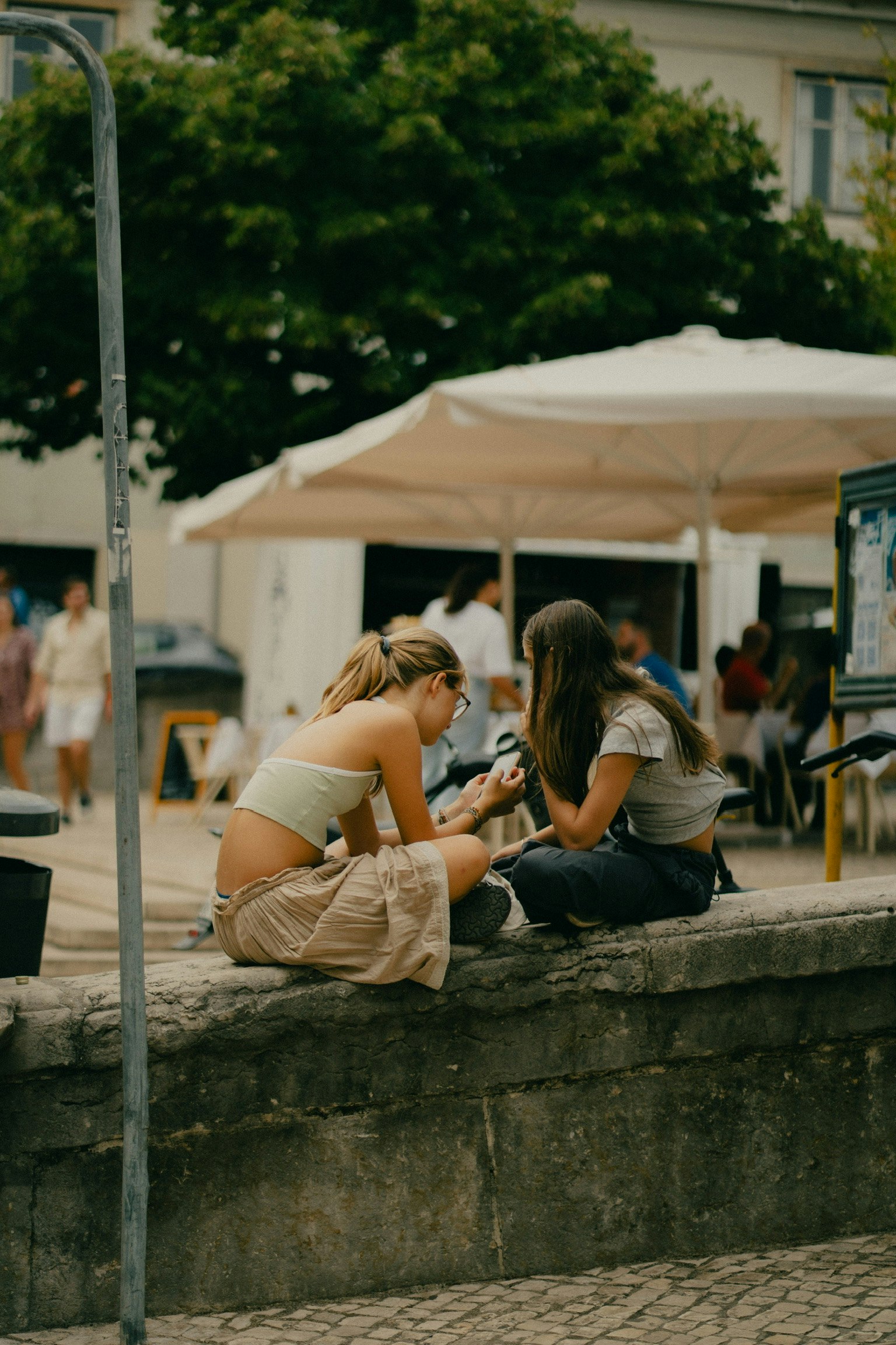 二人の女性が石のベンチに座っている様子 周囲には人々とテントが見える