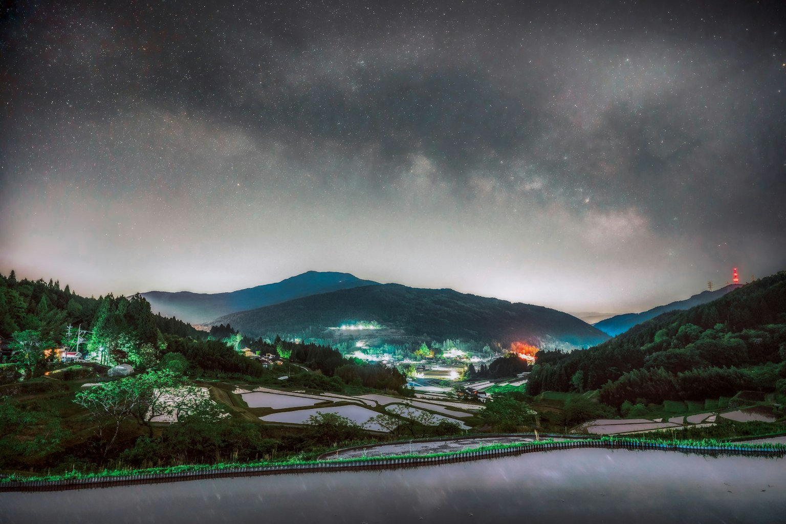 Cielo notturno stellato sopra le montagne e i campi di riso illuminati