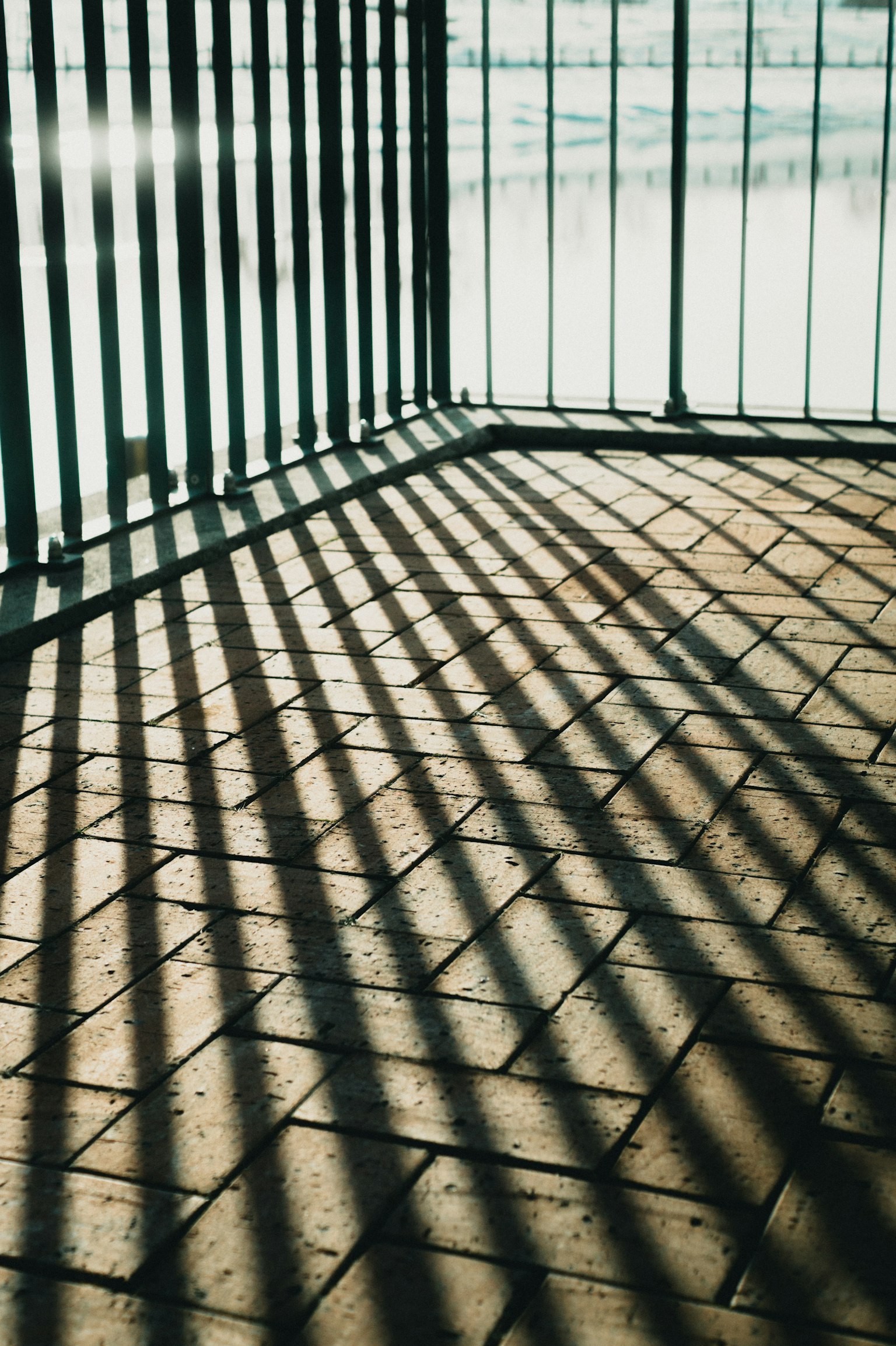 Ecke eines Metallzauns, der gestreifte Schatten auf den Boden wirft