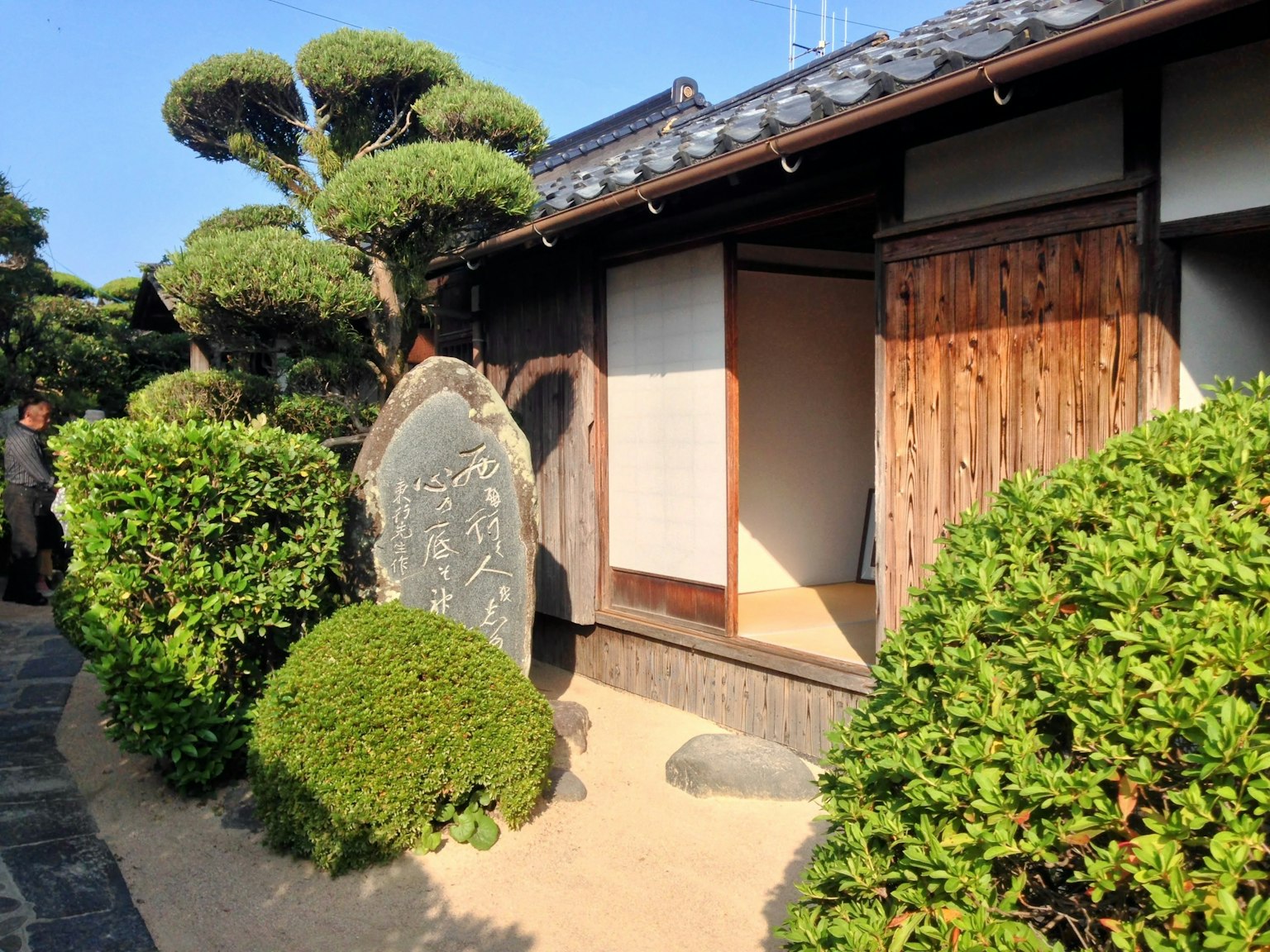 Pemandangan rumah dan taman tradisional Jepang dengan vegetasi rimbun dan monumen batu