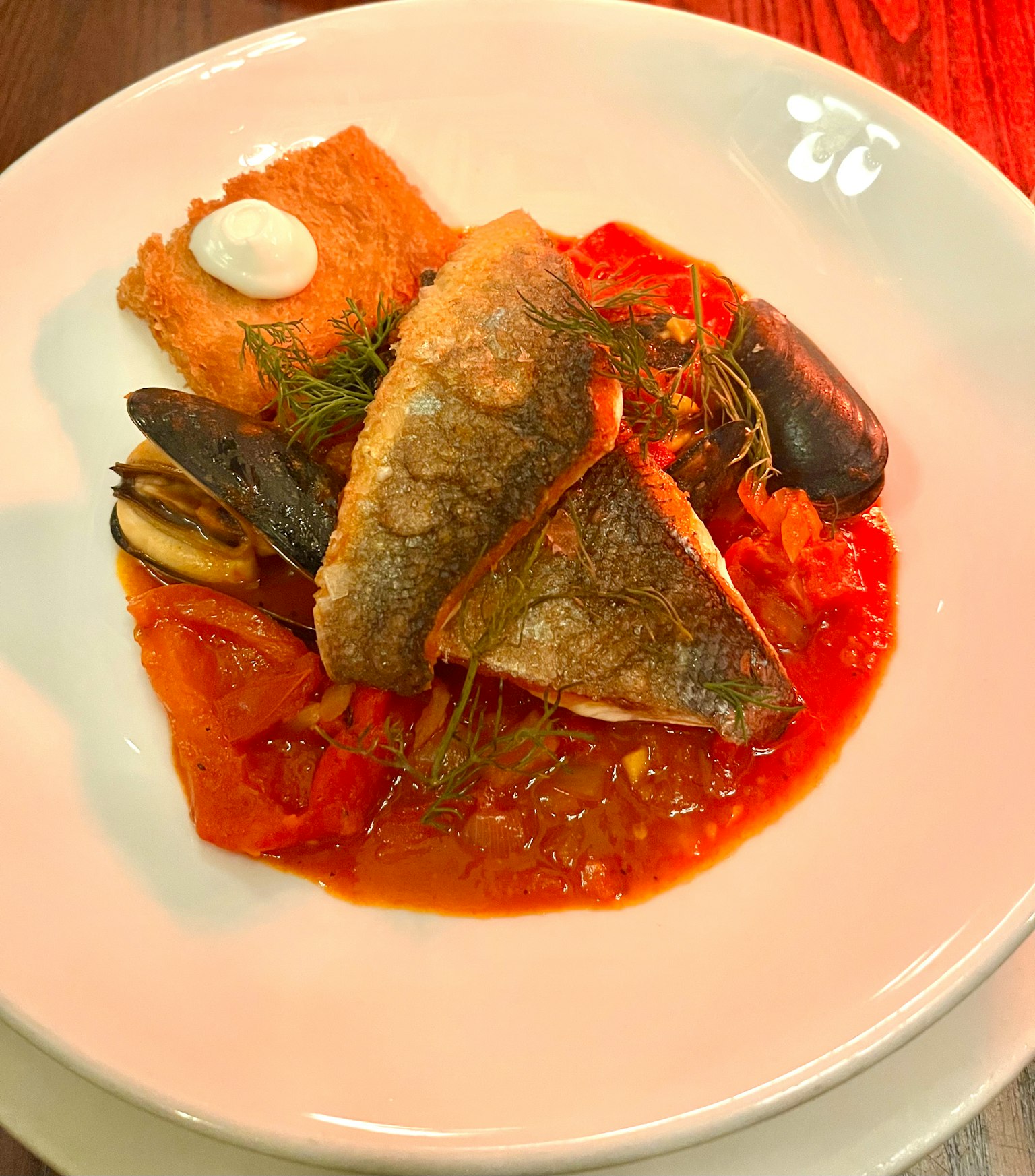 Piatto di pesce delizioso servito su salsa di pomodoro con cozze e erbe