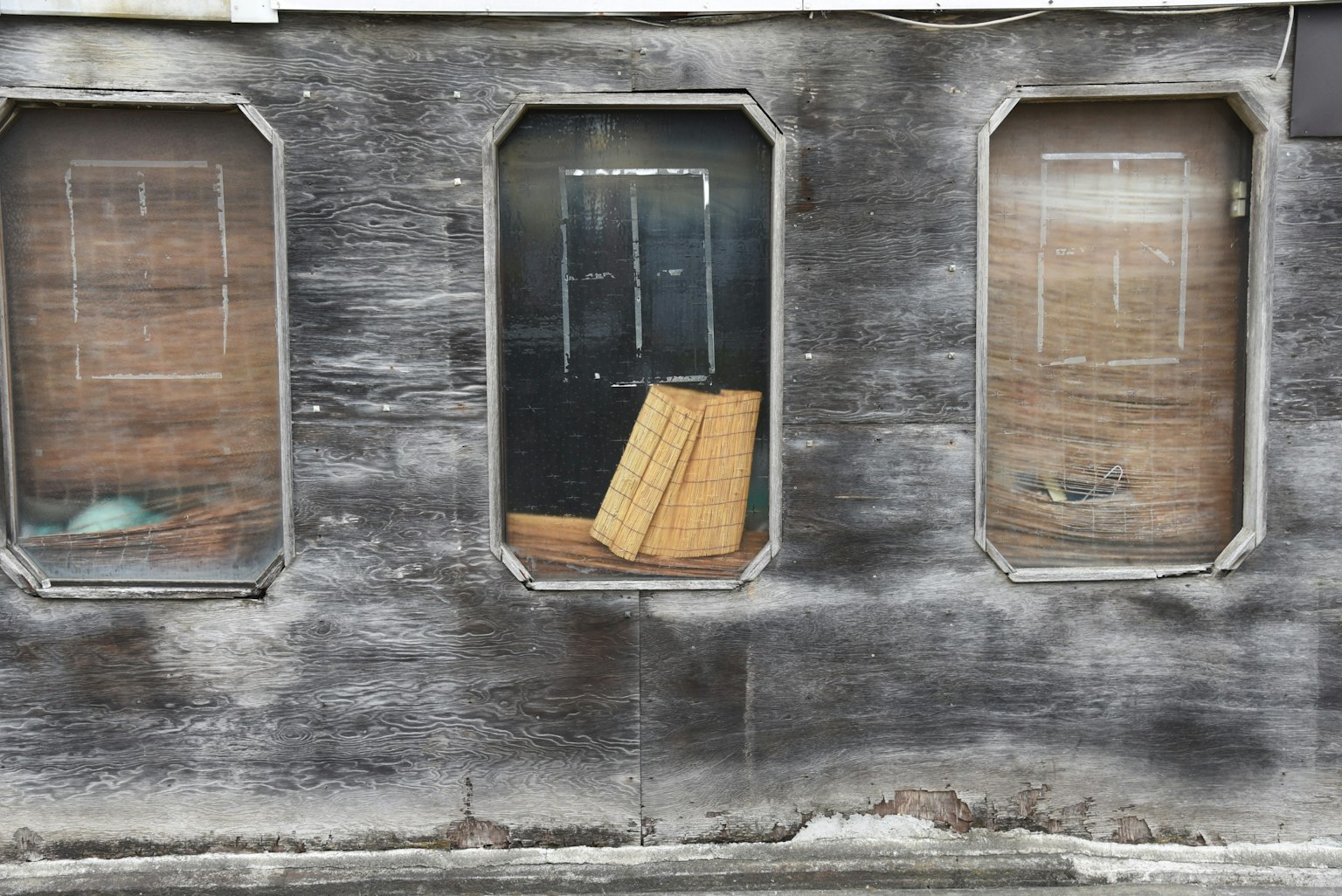 Tres ventanas en la pared de un edificio antiguo con tablones de madera