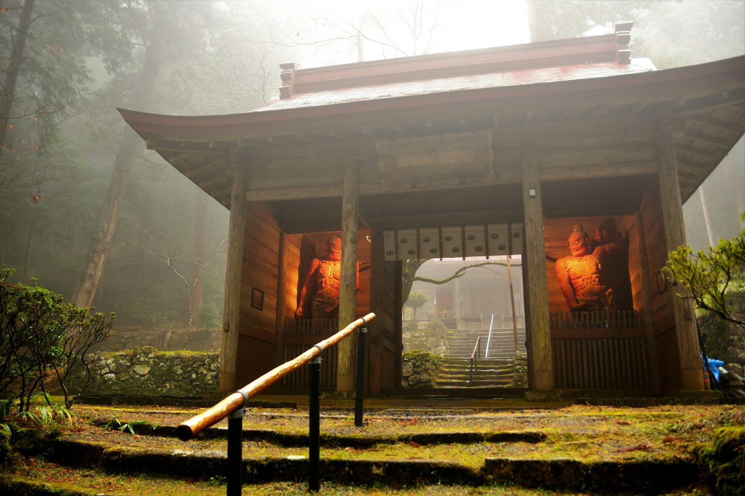 Old shrine gate shrouded in mist with a red roof and warm lights