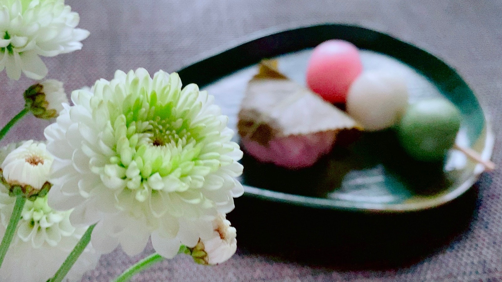 桜餅と三色団子の和菓子、花の添えられた器のある食卓