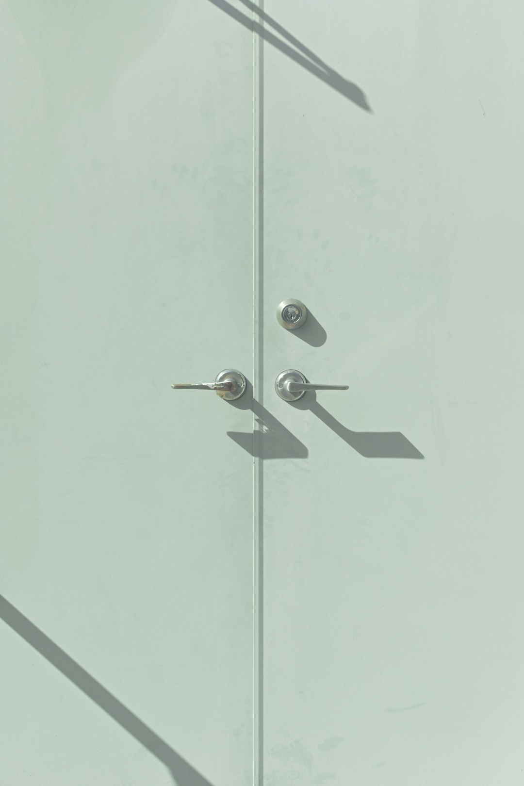 白いドアの上に金属製の取っ手が二つあり影が映っている