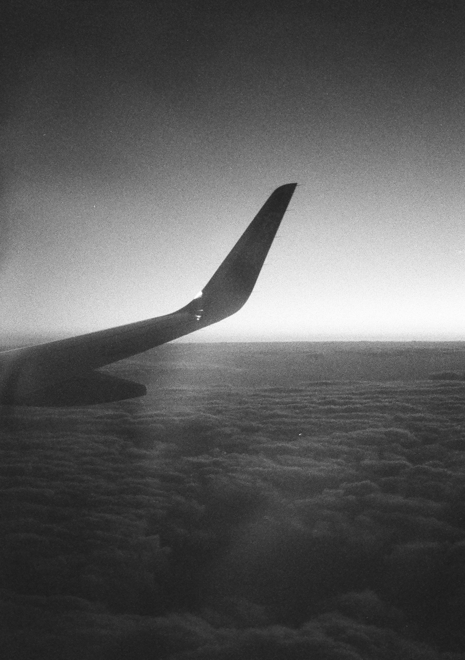 Silhouette of an airplane wing above clouds in black and white