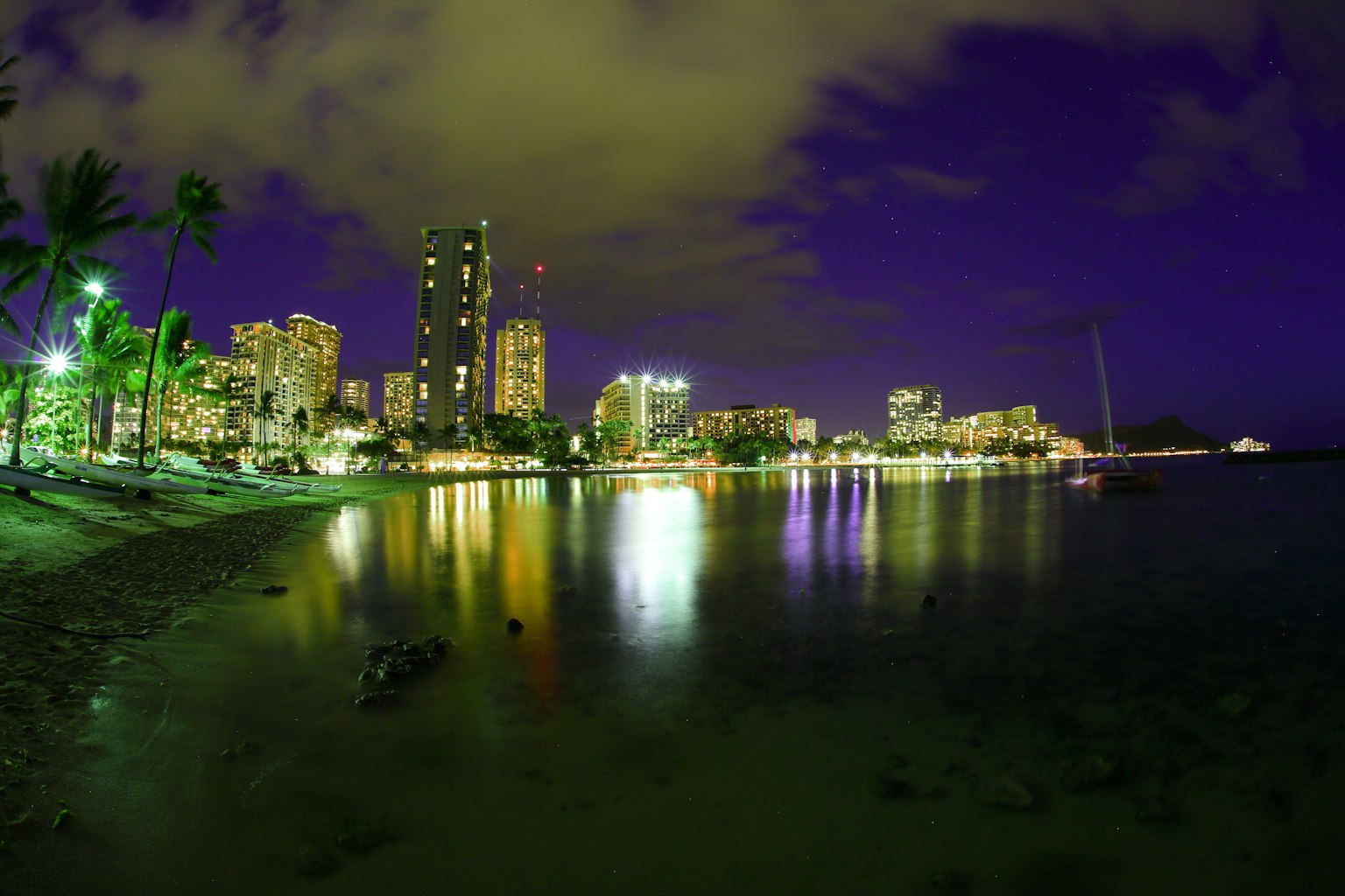 Night view of Honolulu coastline with skyscrapers and reflections