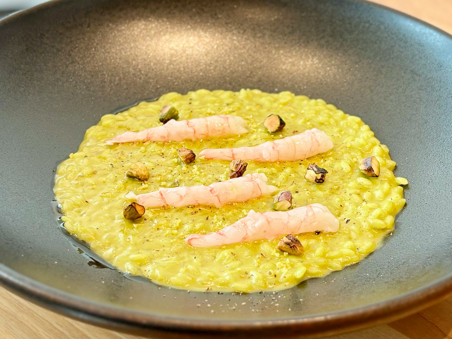 Risotto amarillo cremoso servido en un plato negro con camarones rosados