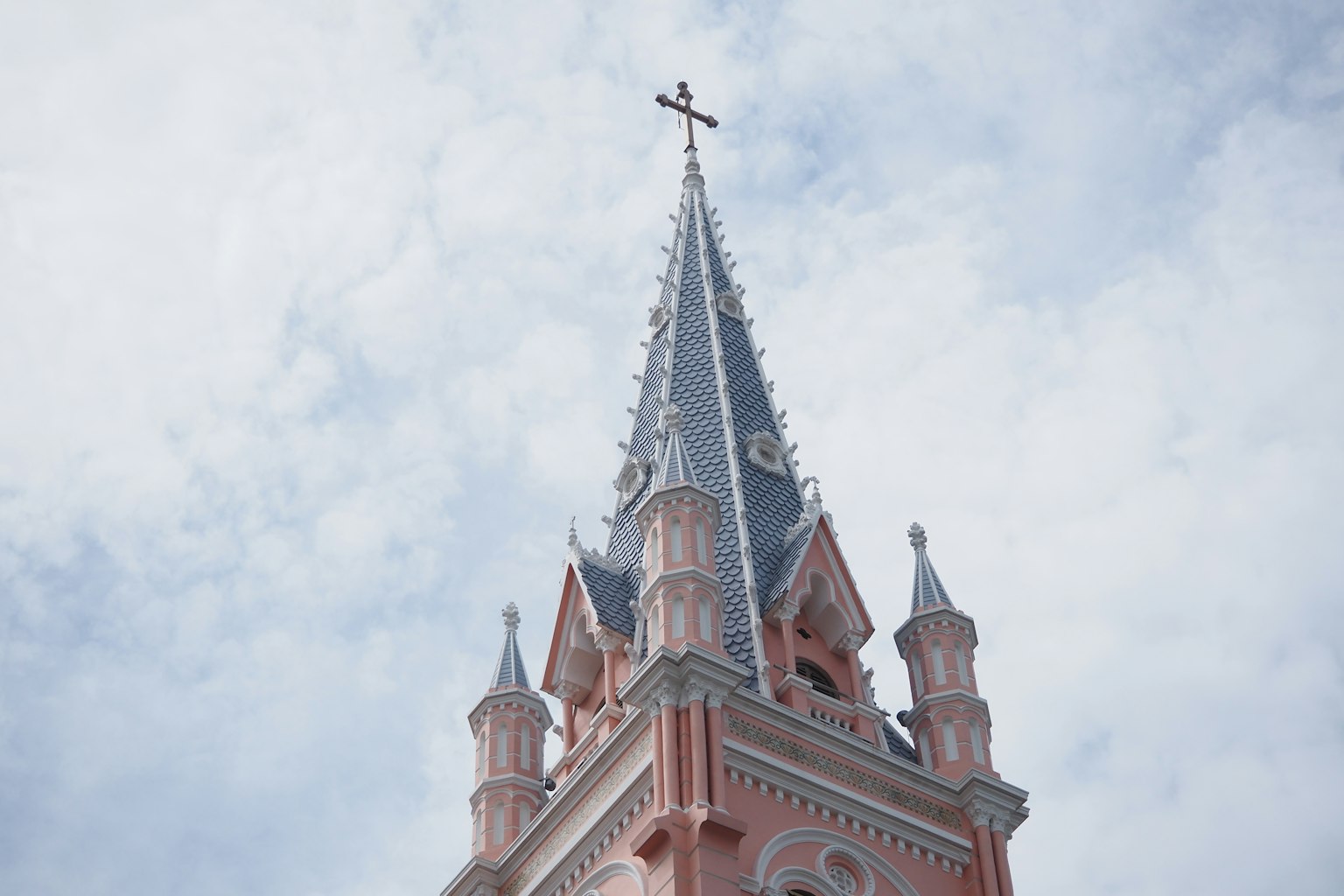 Campanile rosa con croce contro un cielo nuvoloso