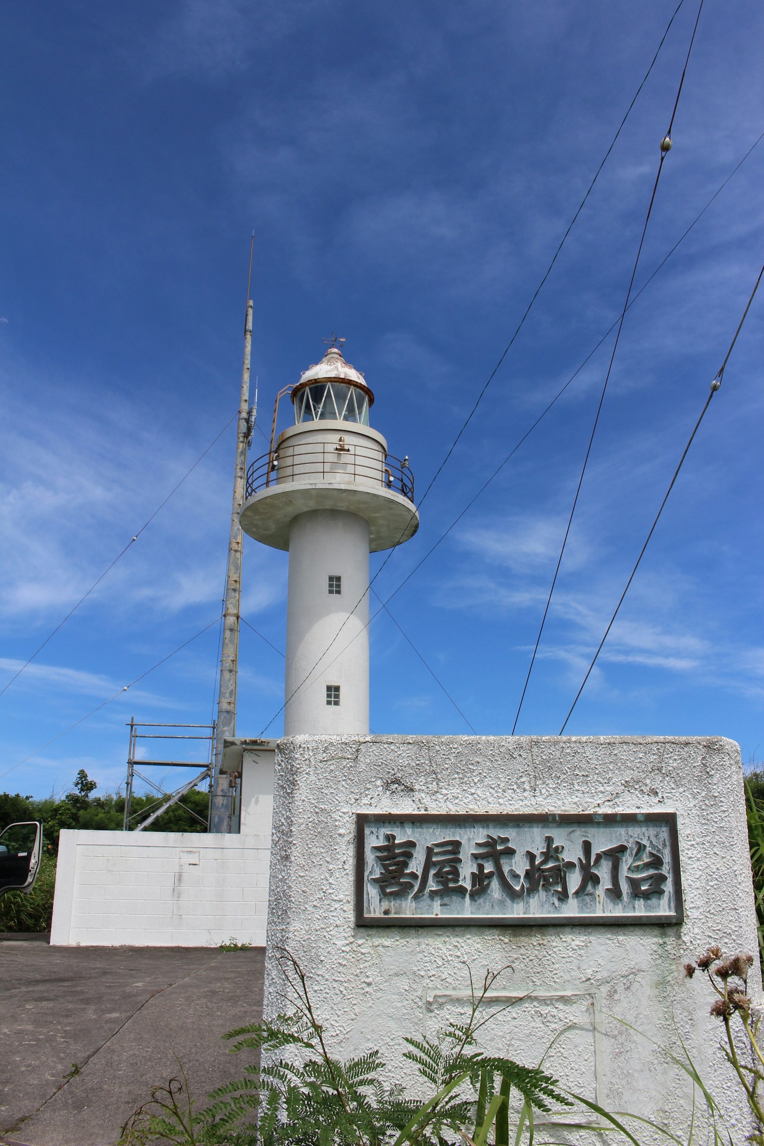 White lighthouse against a blue sky with a sign featuring kanji characters