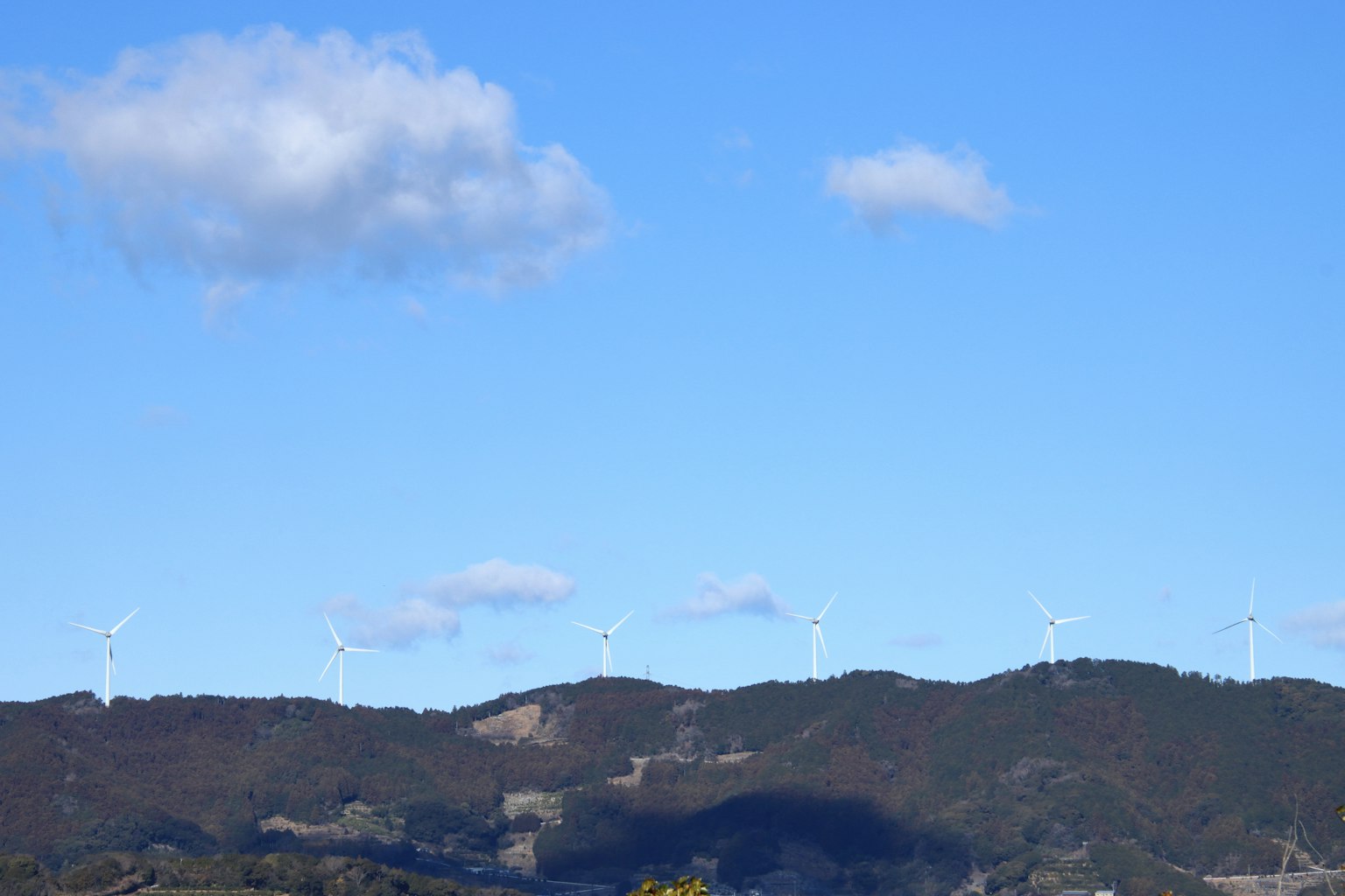 Landscape featuring wind turbines on hills under a clear blue sky