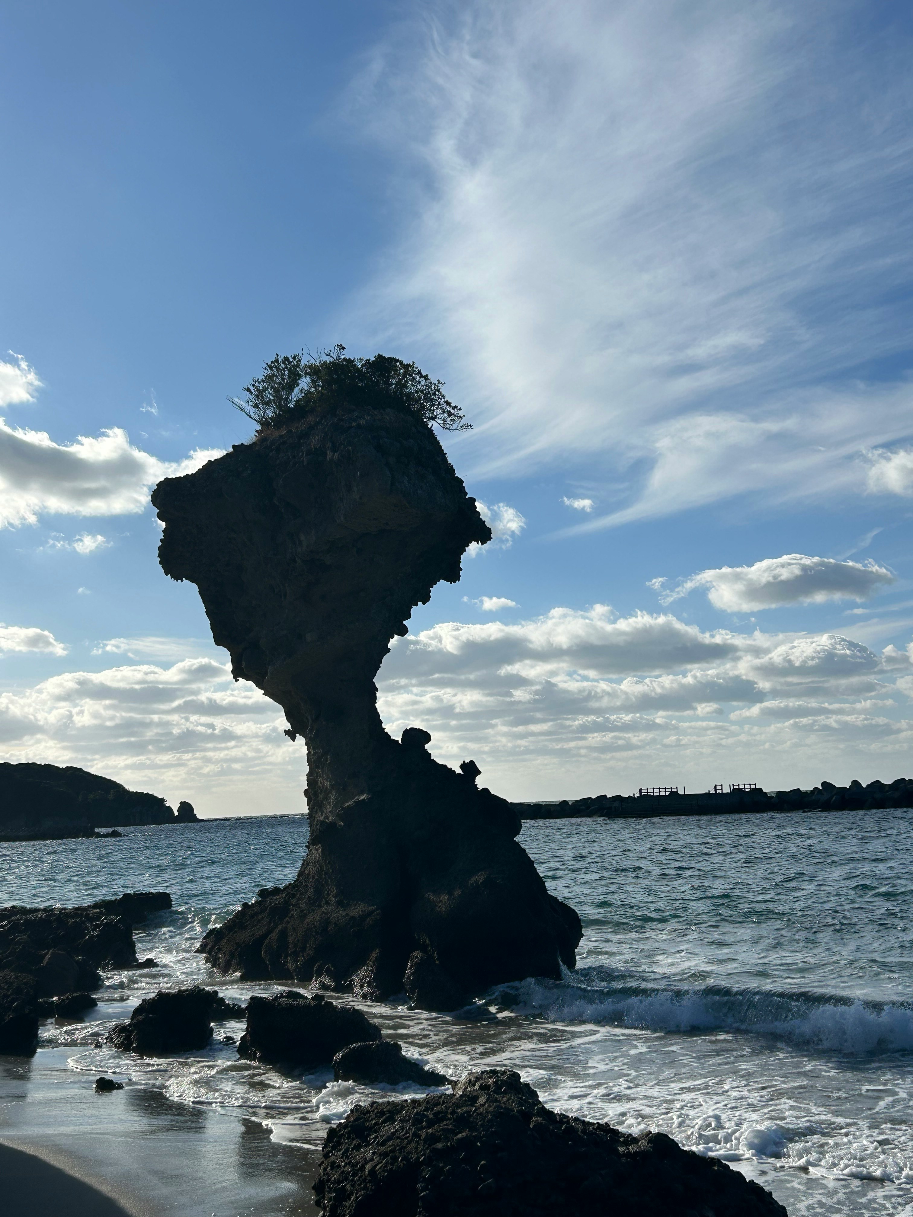 波打ち際に立つ岩のシルエットと青空の海岸風景