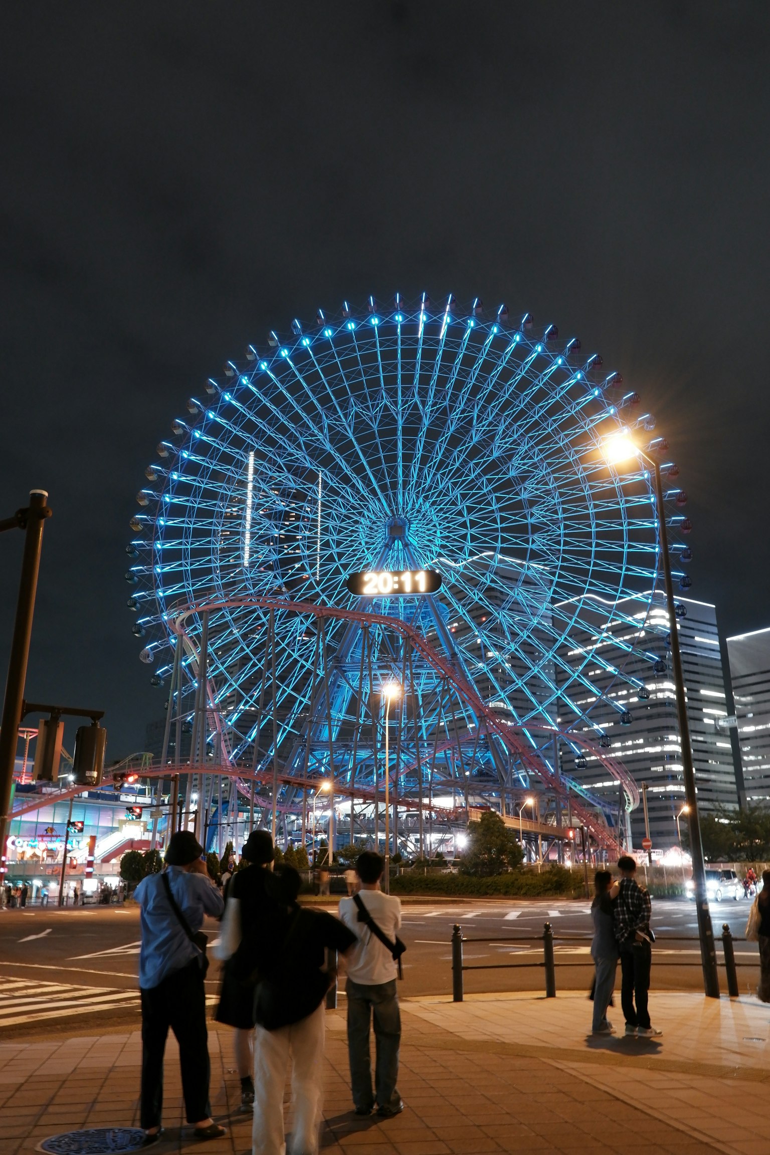 Vue nocturne d'une grande roue illuminée avec des personnes au premier plan