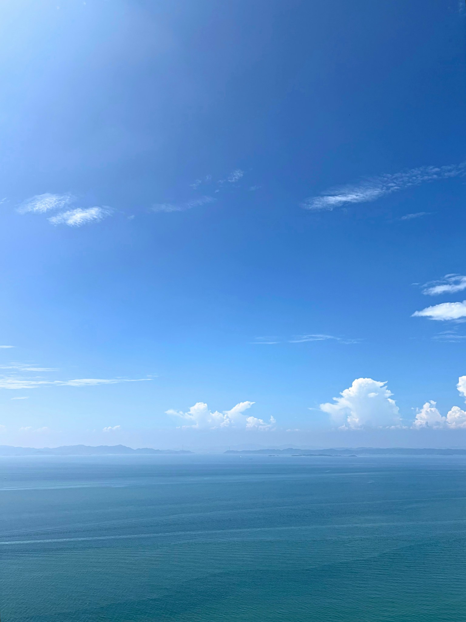 广阔的蓝色海洋在晴朗的蓝天和蓬松的白云下