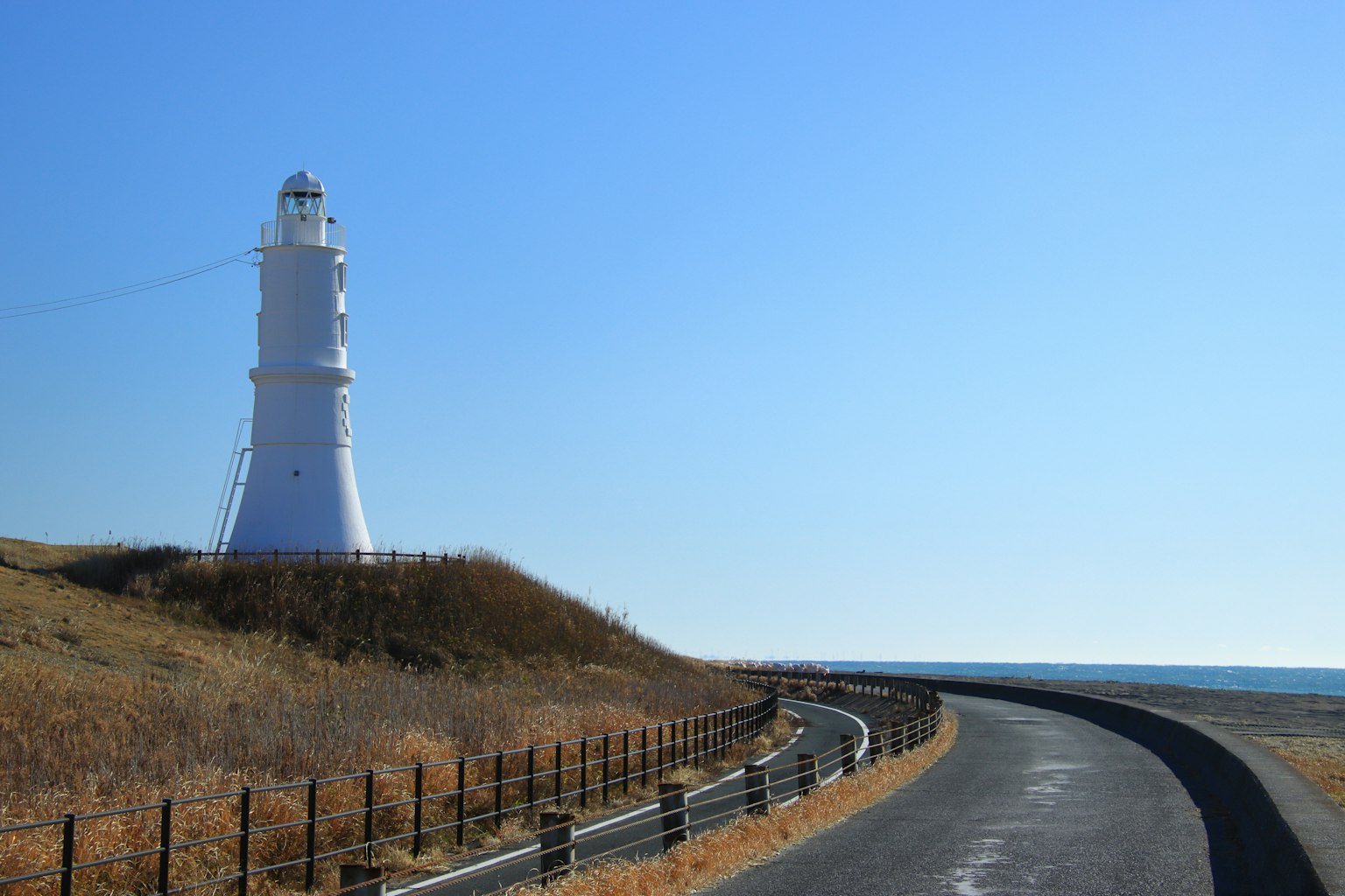 Malerei mit einem weißen Leuchtturm neben einer kurvenreichen Straße unter einem klaren blauen Himmel