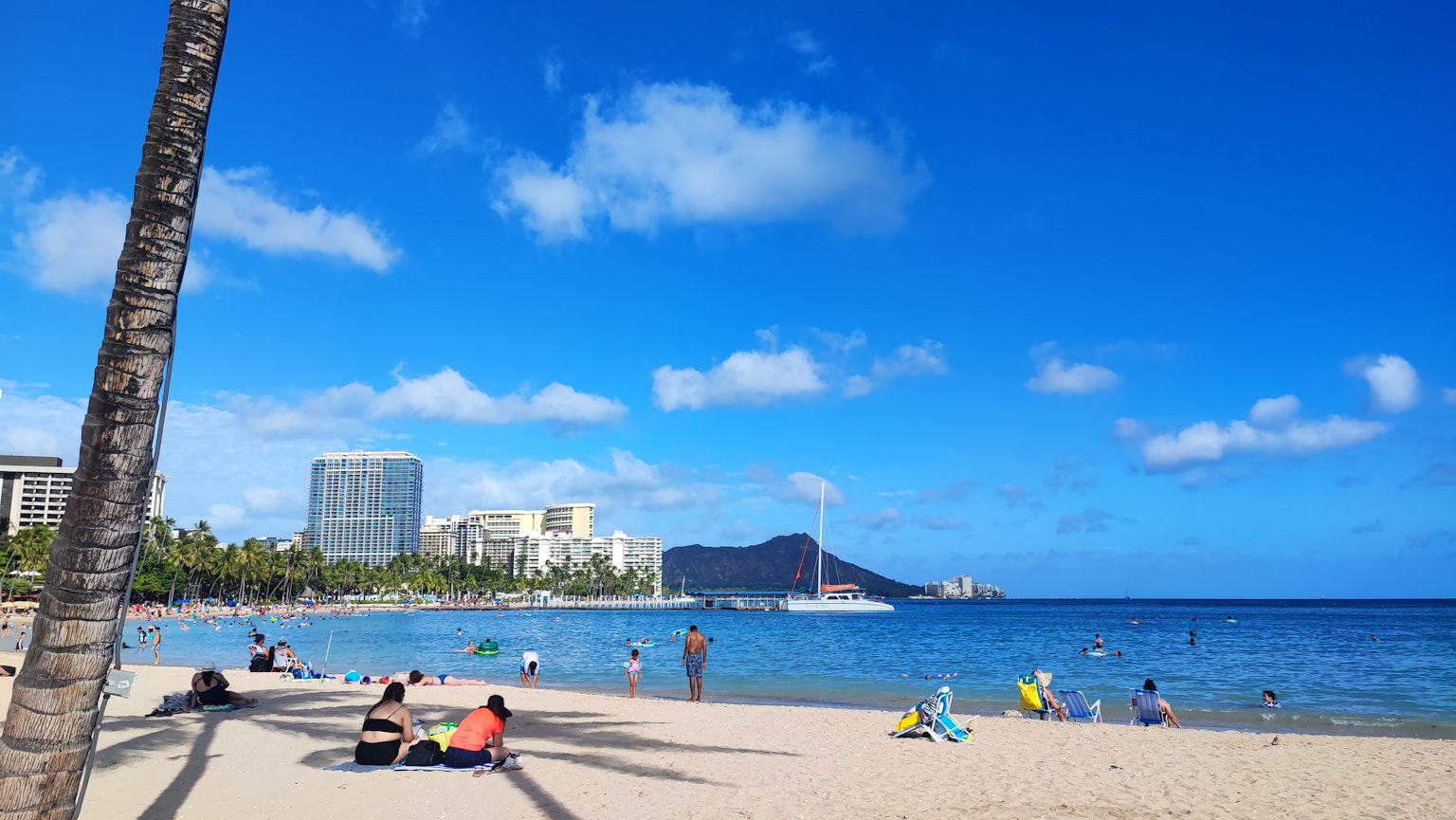 Orang-orang bersantai di pantai Hawaii dengan laut dan langit biru