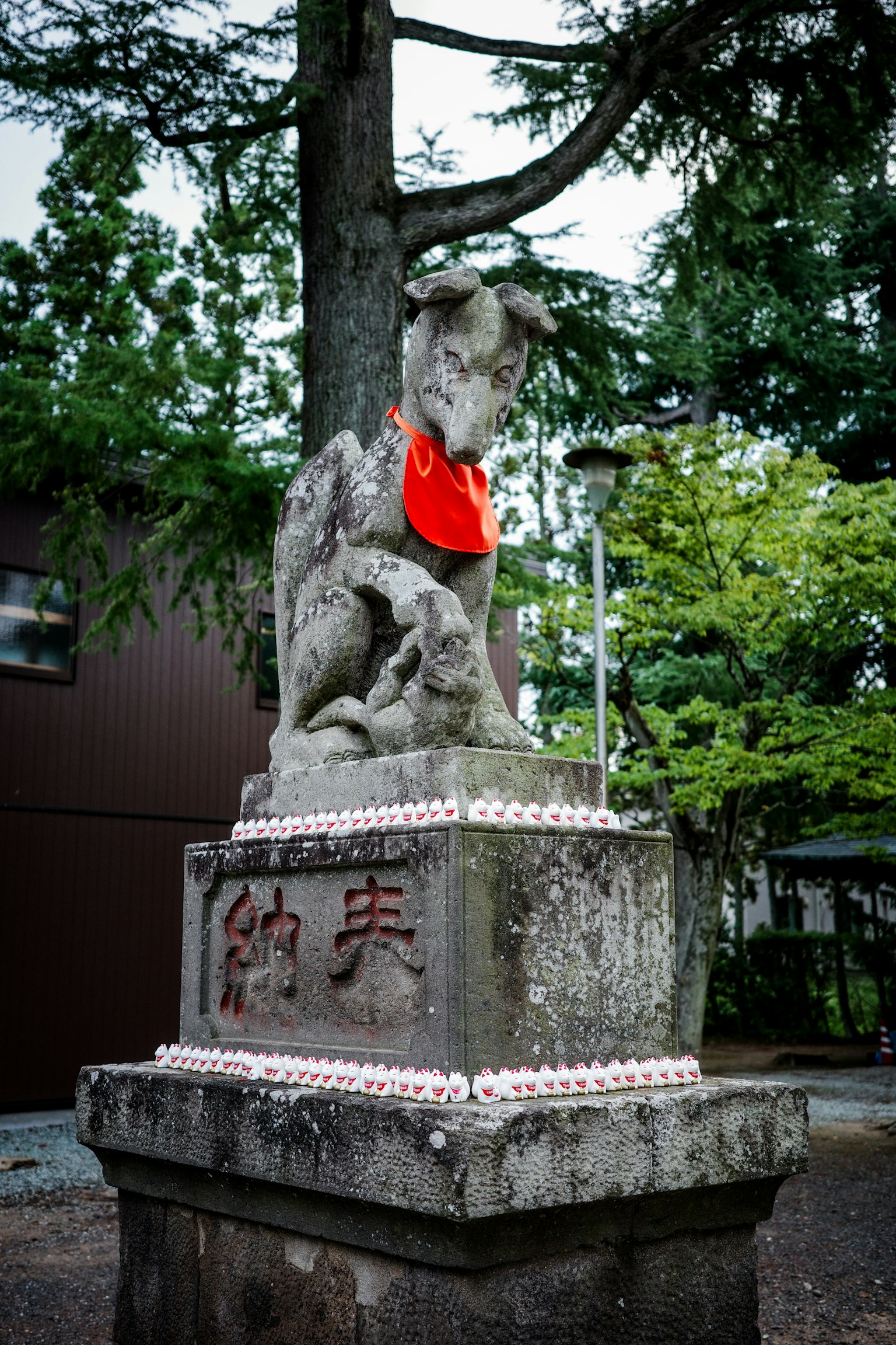 Statue en pierre d'un chien gardien portant une écharpe rouge près d'un arbre