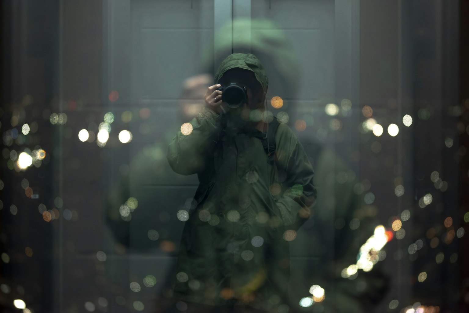 Reflection of a person with a camera in an elevator mirror with blurred city lights