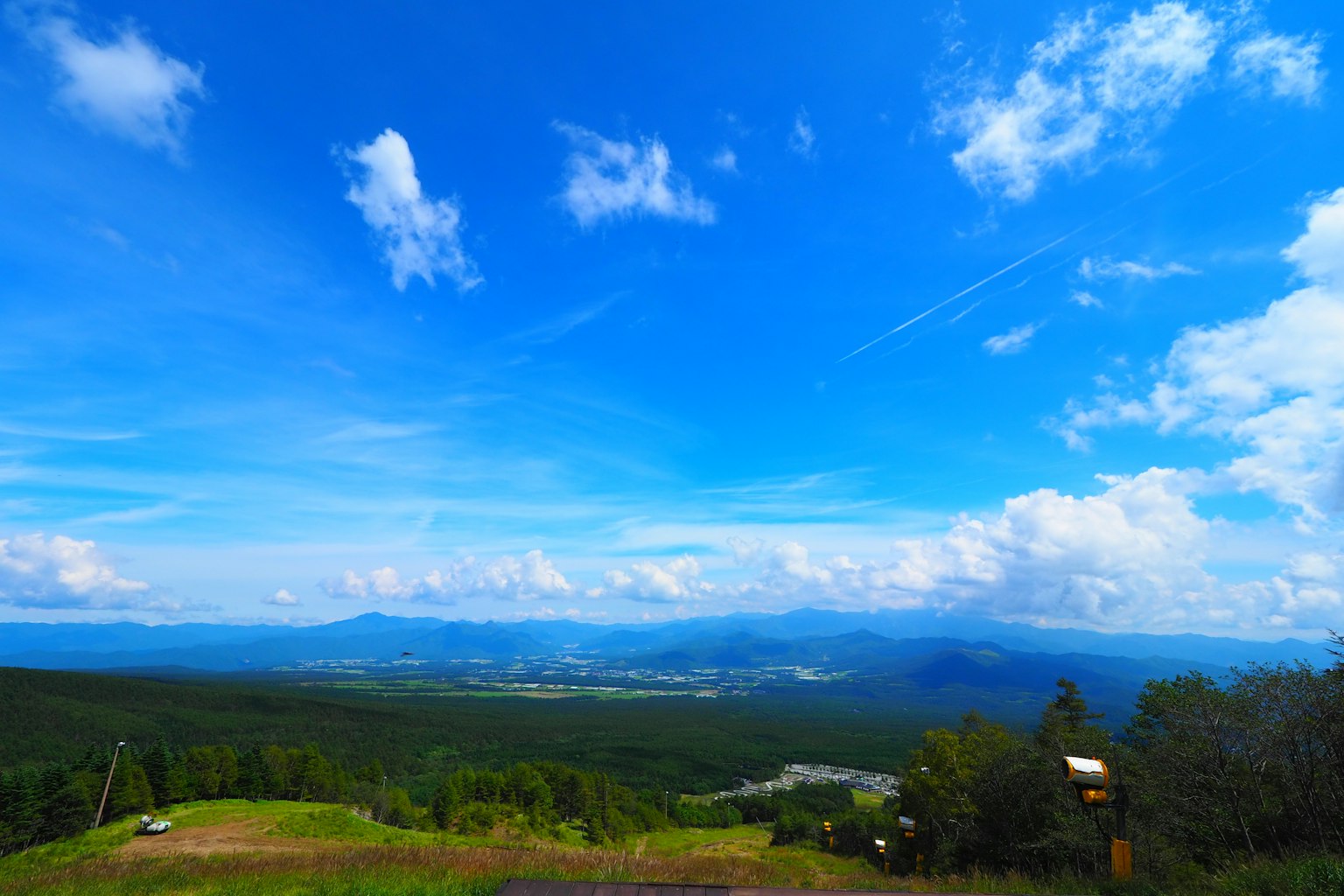 Panoramablick auf einen blauen Himmel mit Wolken über grünen Hügeln und entfernten Bergen