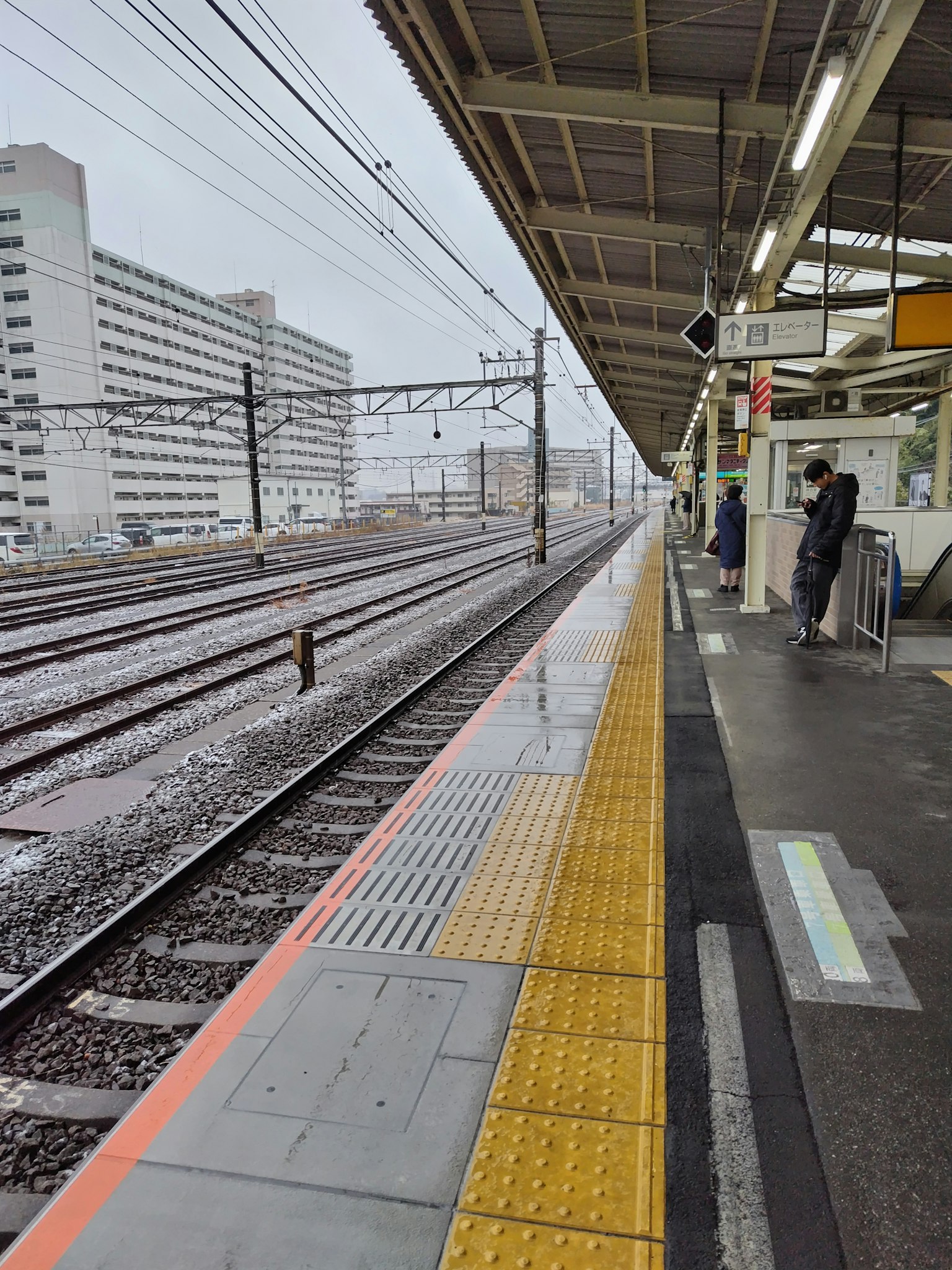 ชานชาลาสถานีรถไฟในวันที่ฝนตกพร้อมรางรถไฟที่มองเห็นได้