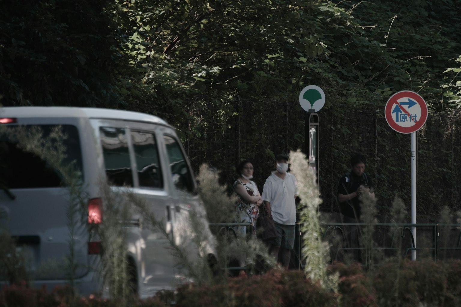 Escena con varias personas de pie al borde de la carretera junto a un vehículo y señales de tráfico