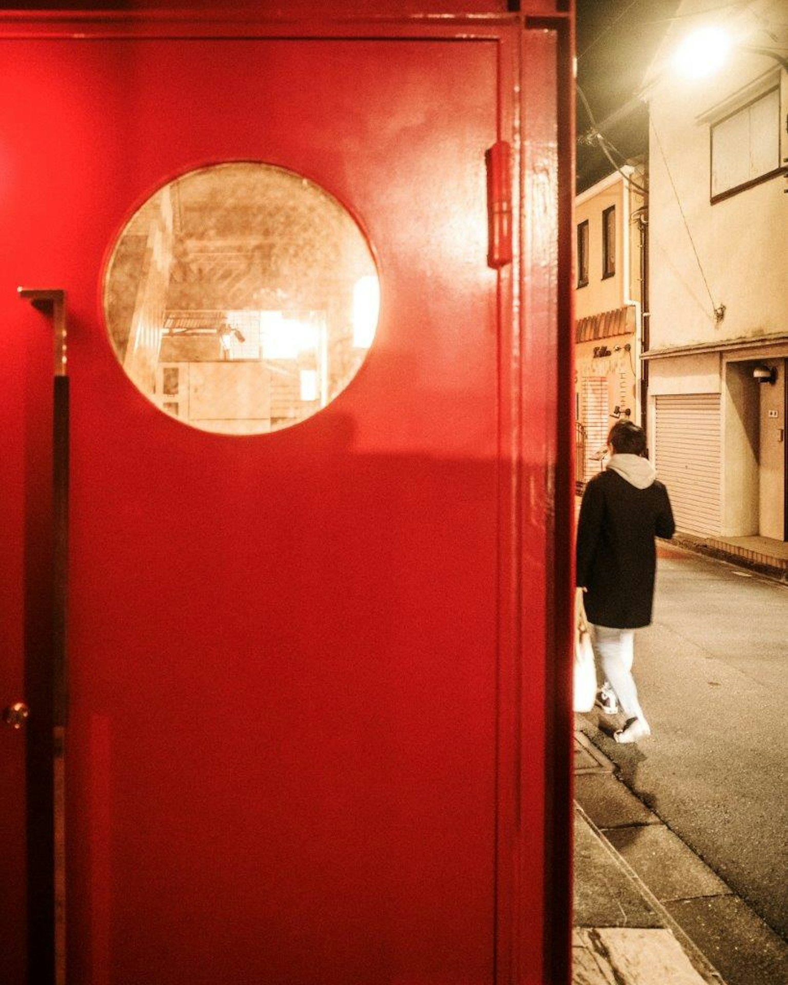 Porta rossa con una finestra rotonda accanto a una persona che cammina nella strada di notte