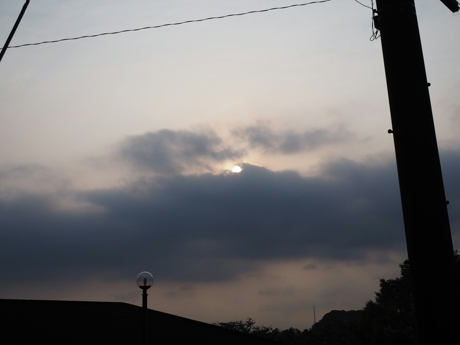 Sole parzialmente nascosto dalle nuvole con un palo della luce in silhouette