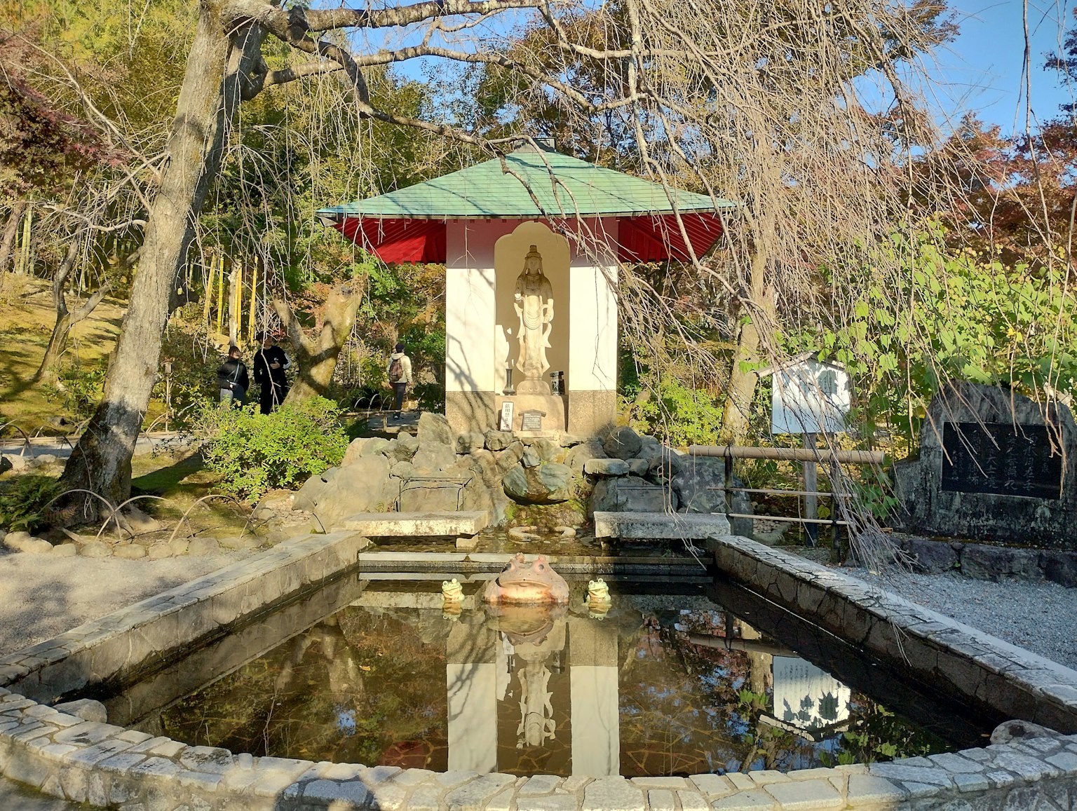 Scena di giardino con un piccolo padiglione dal tetto verde e una statua riflessa nell'acqua
