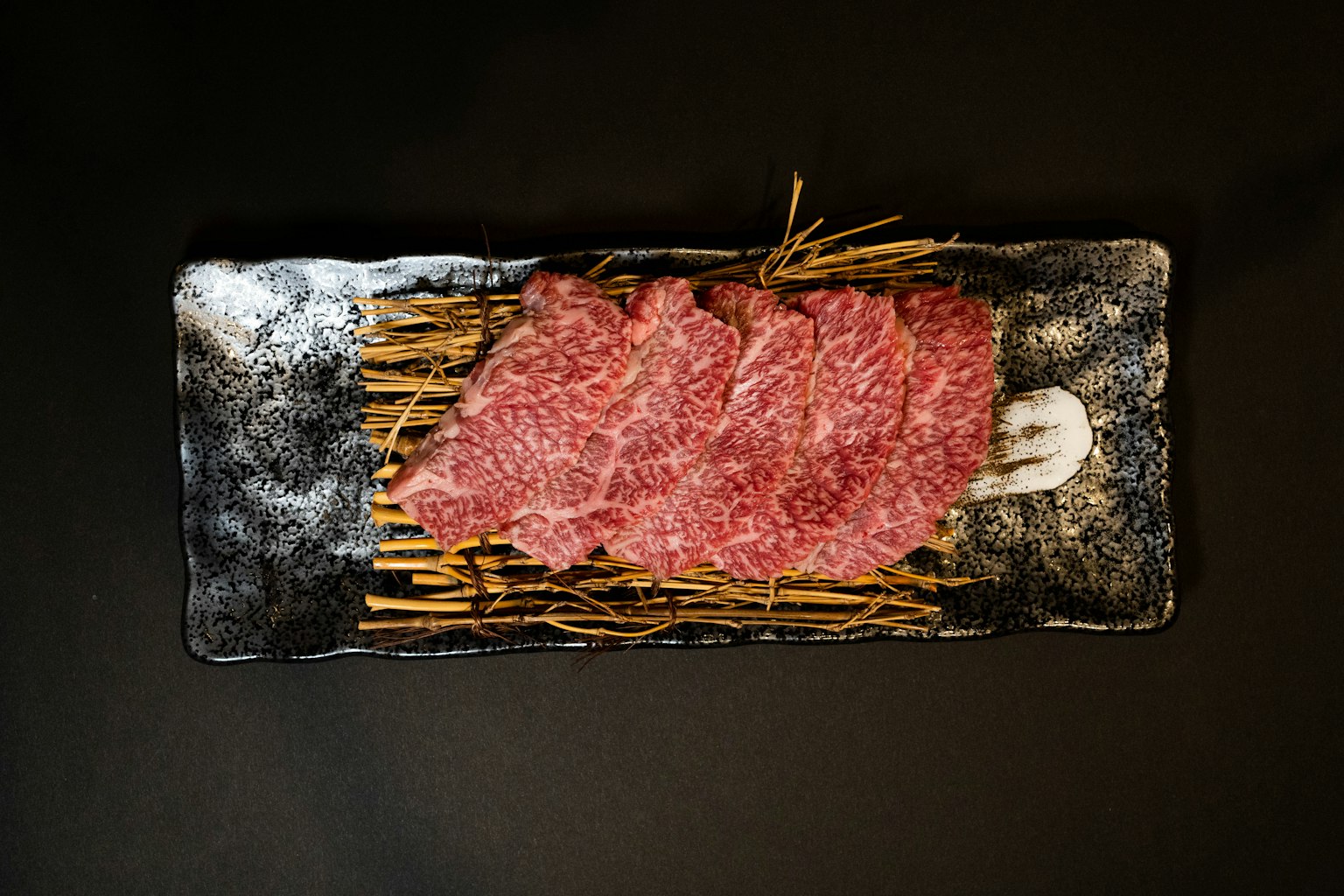 Viande tranchée finement présentée sur un fond noir avec des bâtons de bambou