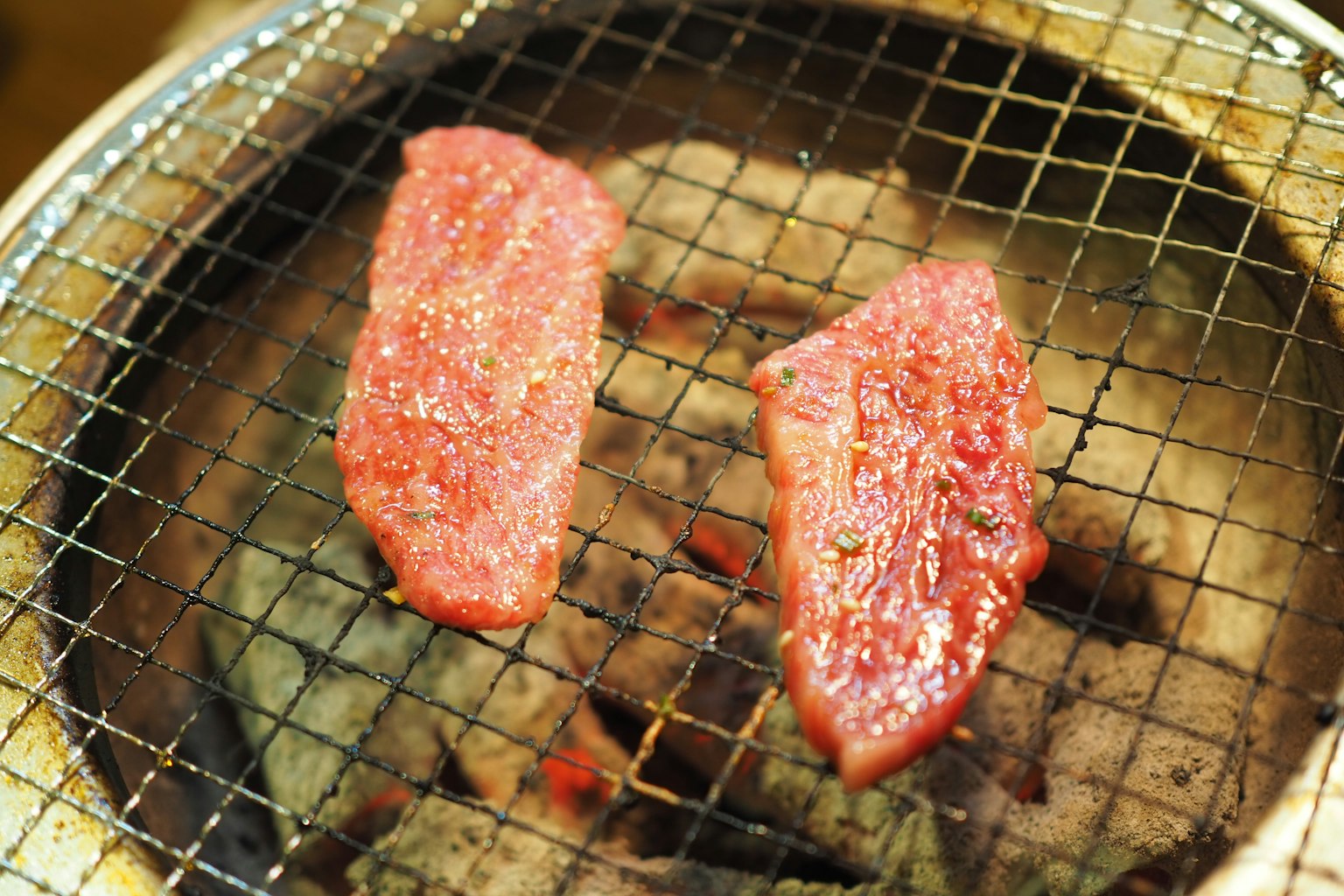Slices of meat grilling on a wire mesh over hot coals