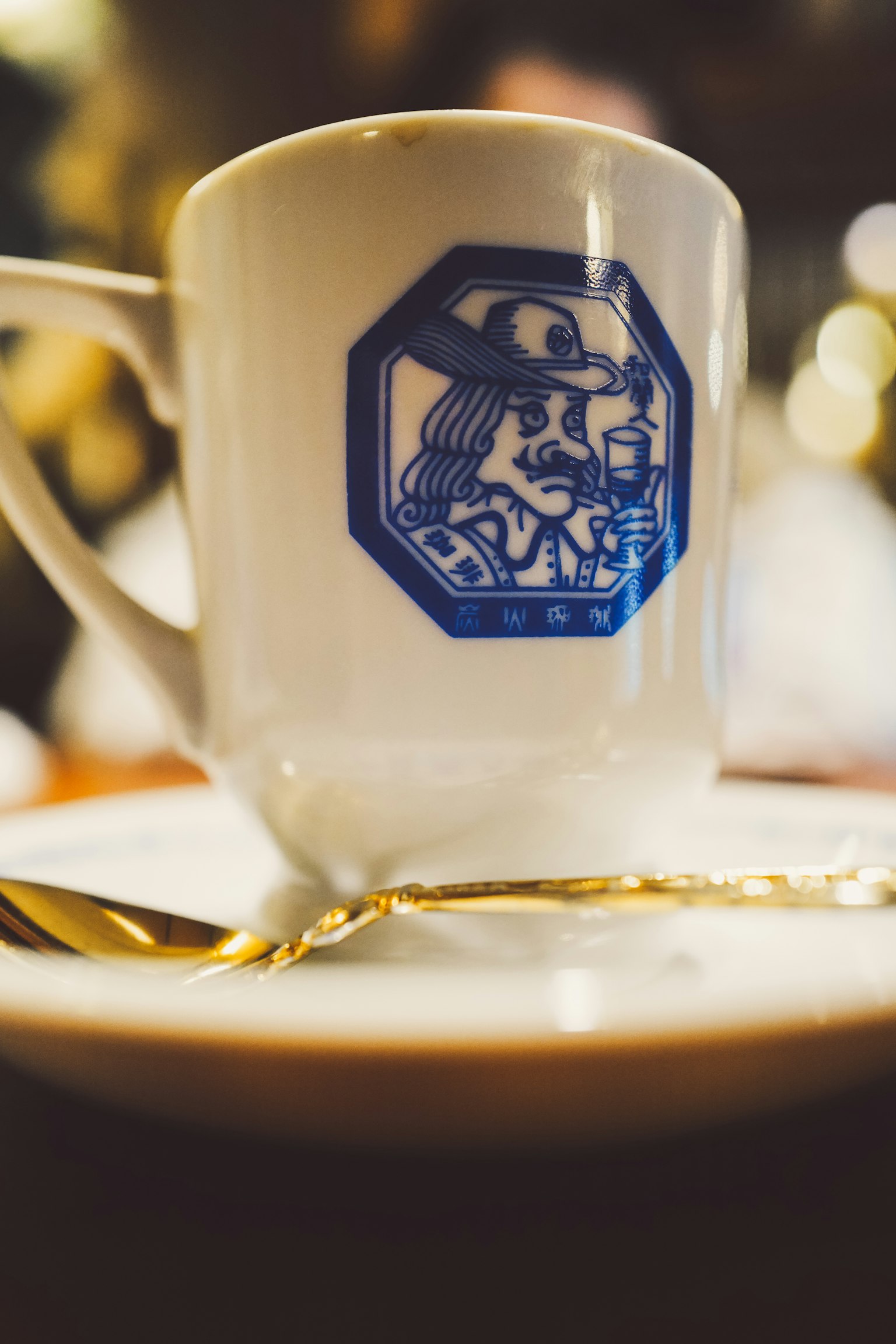 白色咖啡杯帶藍色圖案和金色湯匙在盤子上