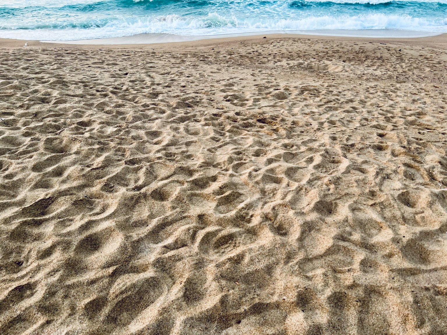 Gros plan de la plage de sable au bord de l'eau avec des vagues bleues visibles