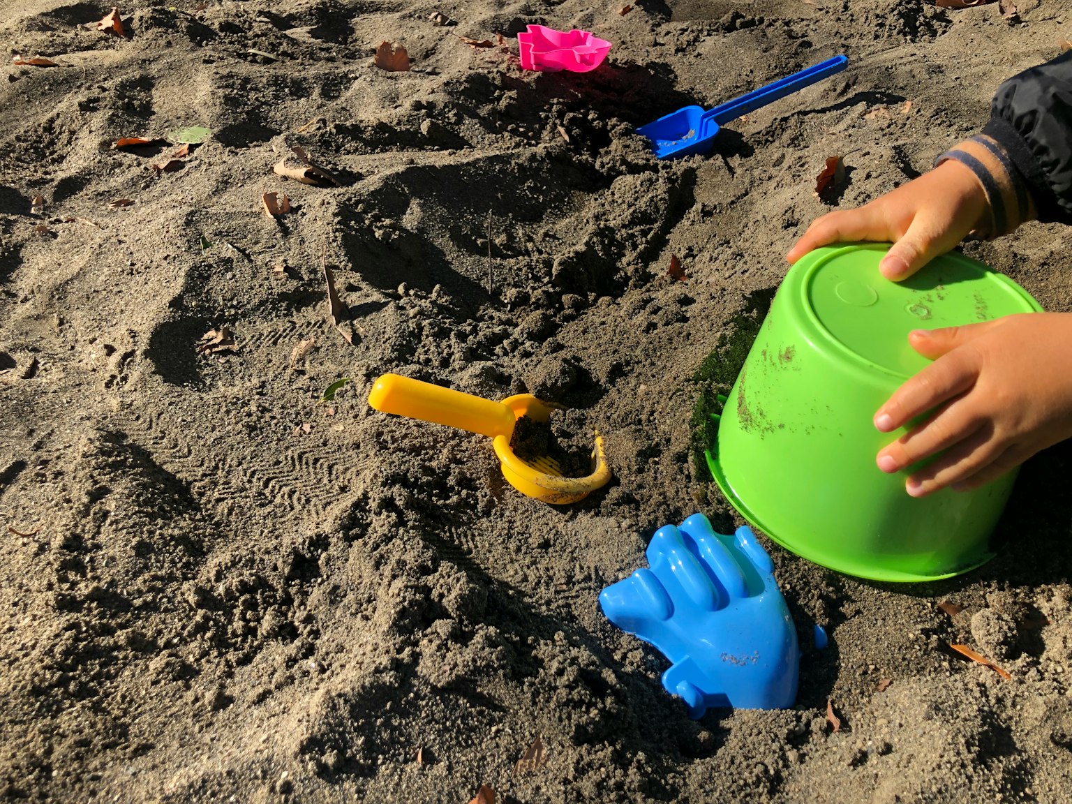 Mani di un bambino che gioca nella sabbia con giocattoli colorati