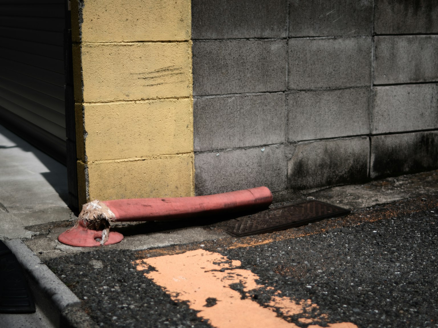 Tubo rosso appoggiato contro un angolo di muro in cemento con un tombino