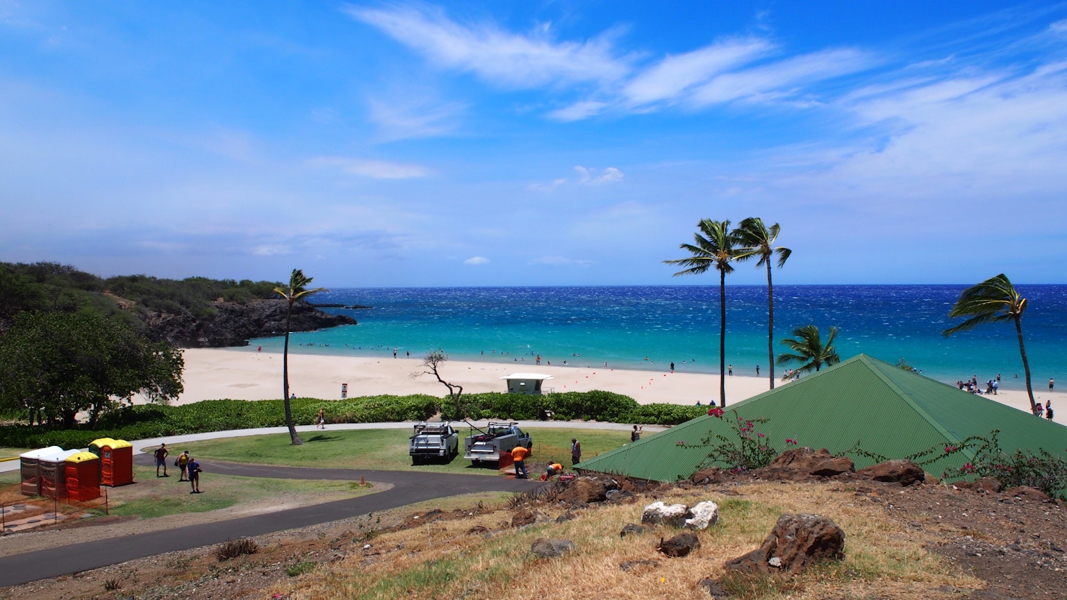 Scenic beach view with blue ocean and white sand green hill and palm trees