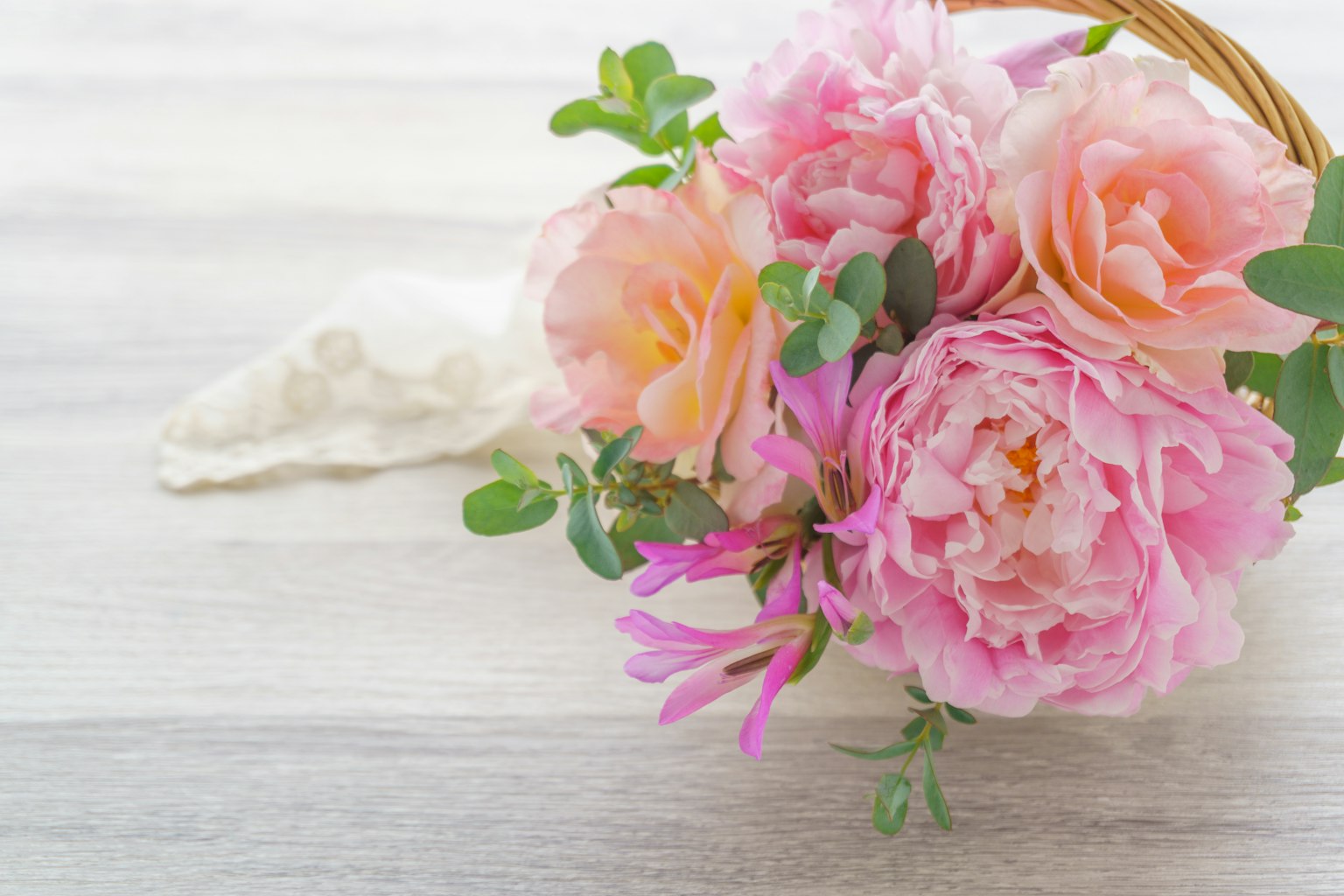 A bouquet of pink roses and green leaves is placed on a wooden table