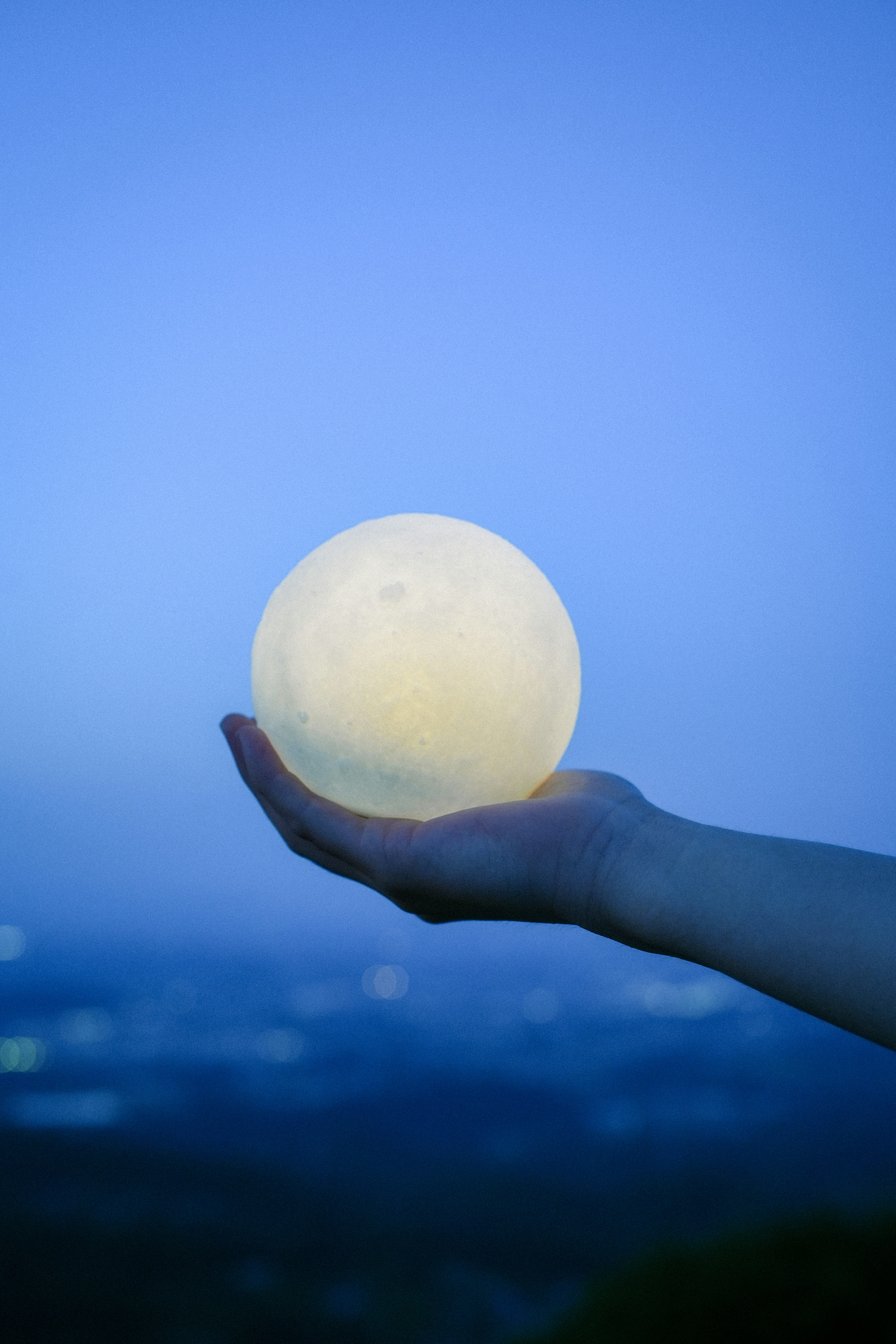 青空の下で手のひらに浮かぶ白い球体の幻想的な光