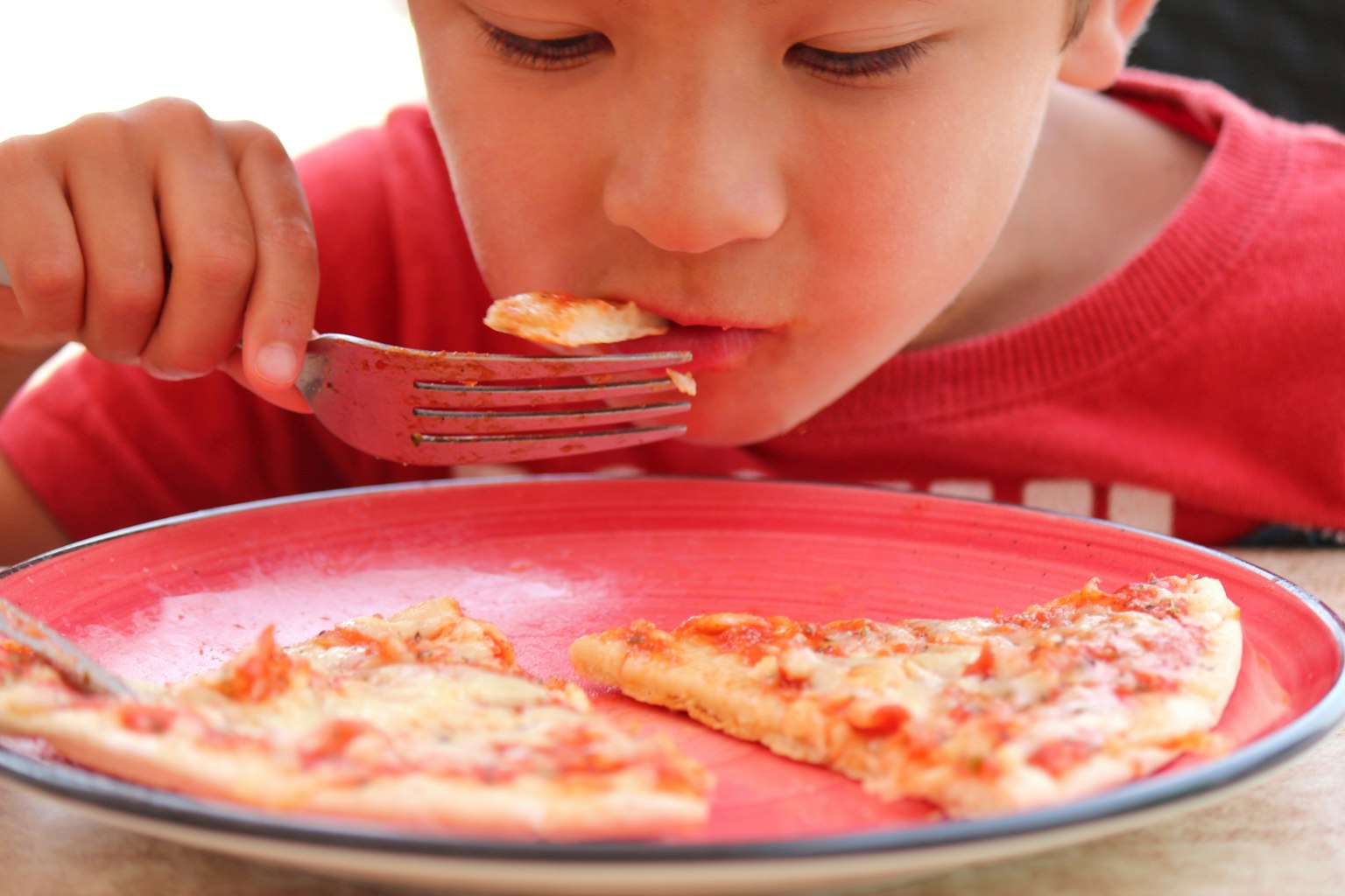 Un bambino che mangia una pizza con una maglietta rossa