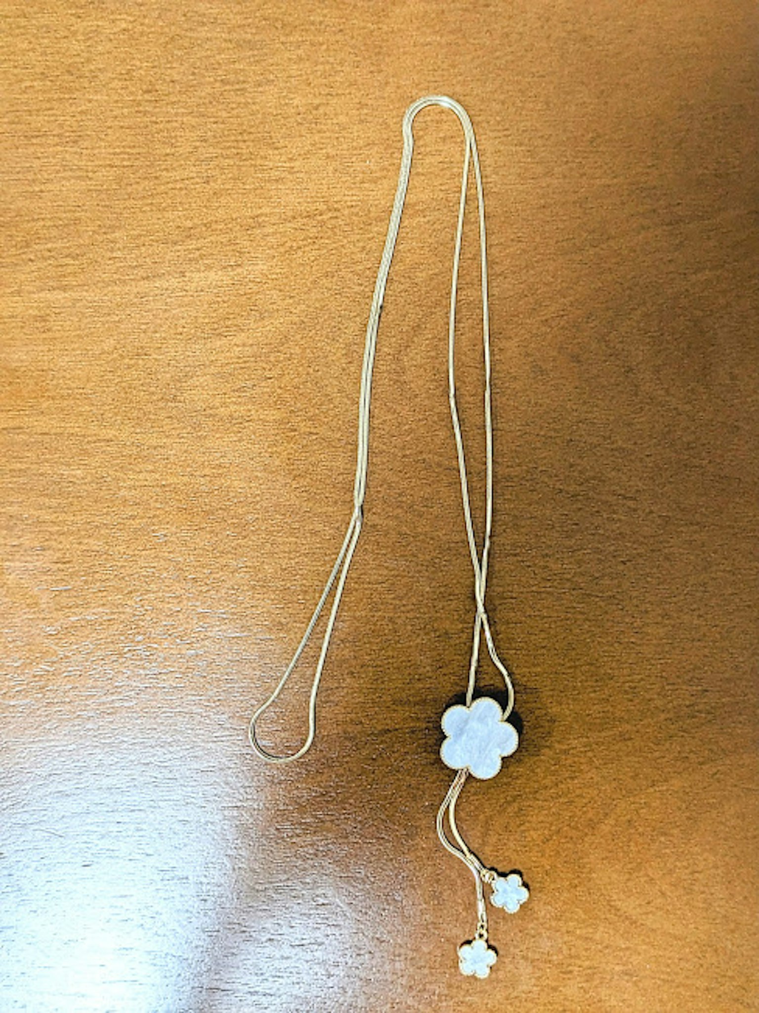 Una collana con un motivo di fiore bianco appoggiata su un tavolo di legno