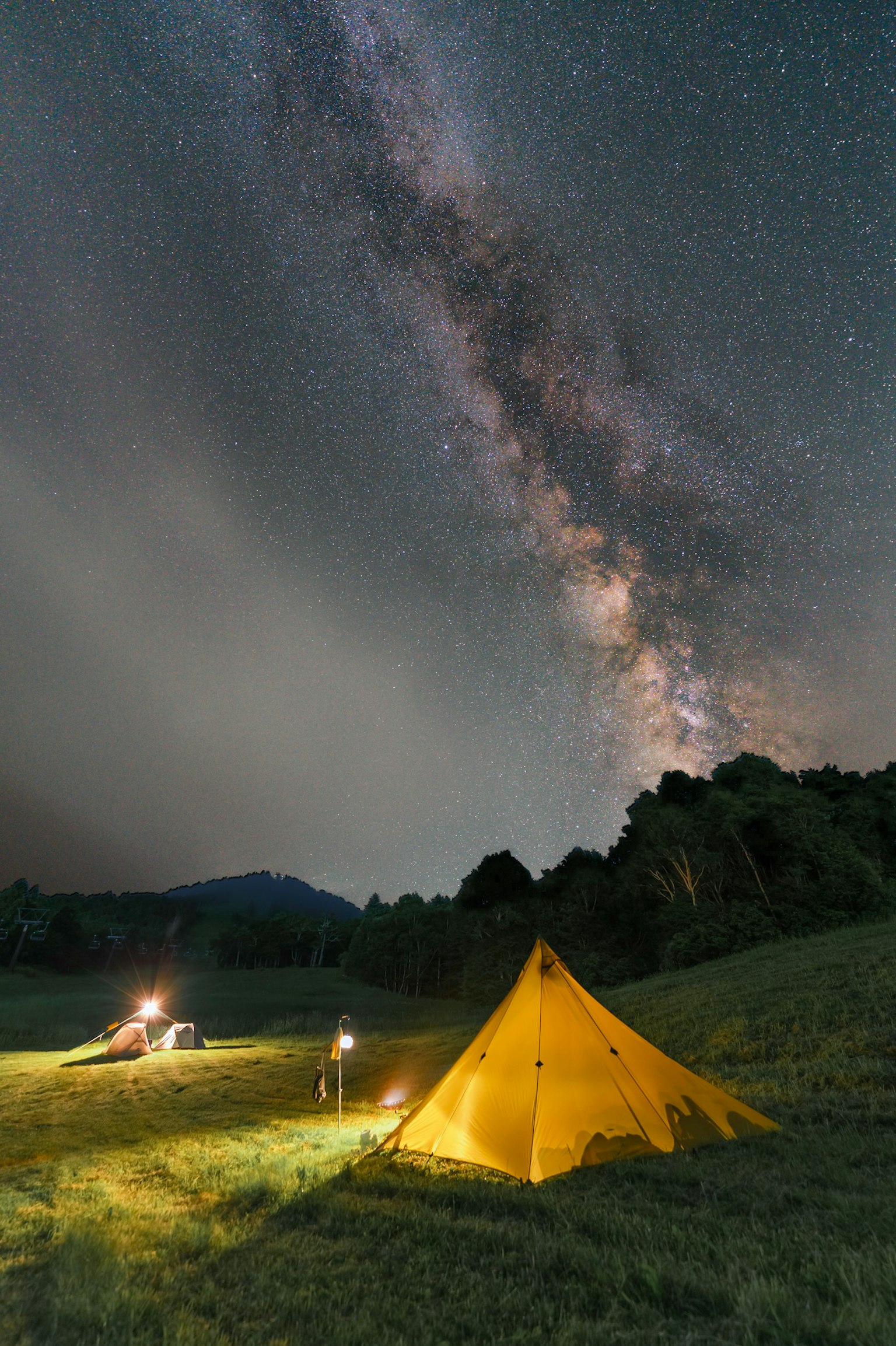 Personas acampando bajo un cielo estrellado con una tienda amarilla