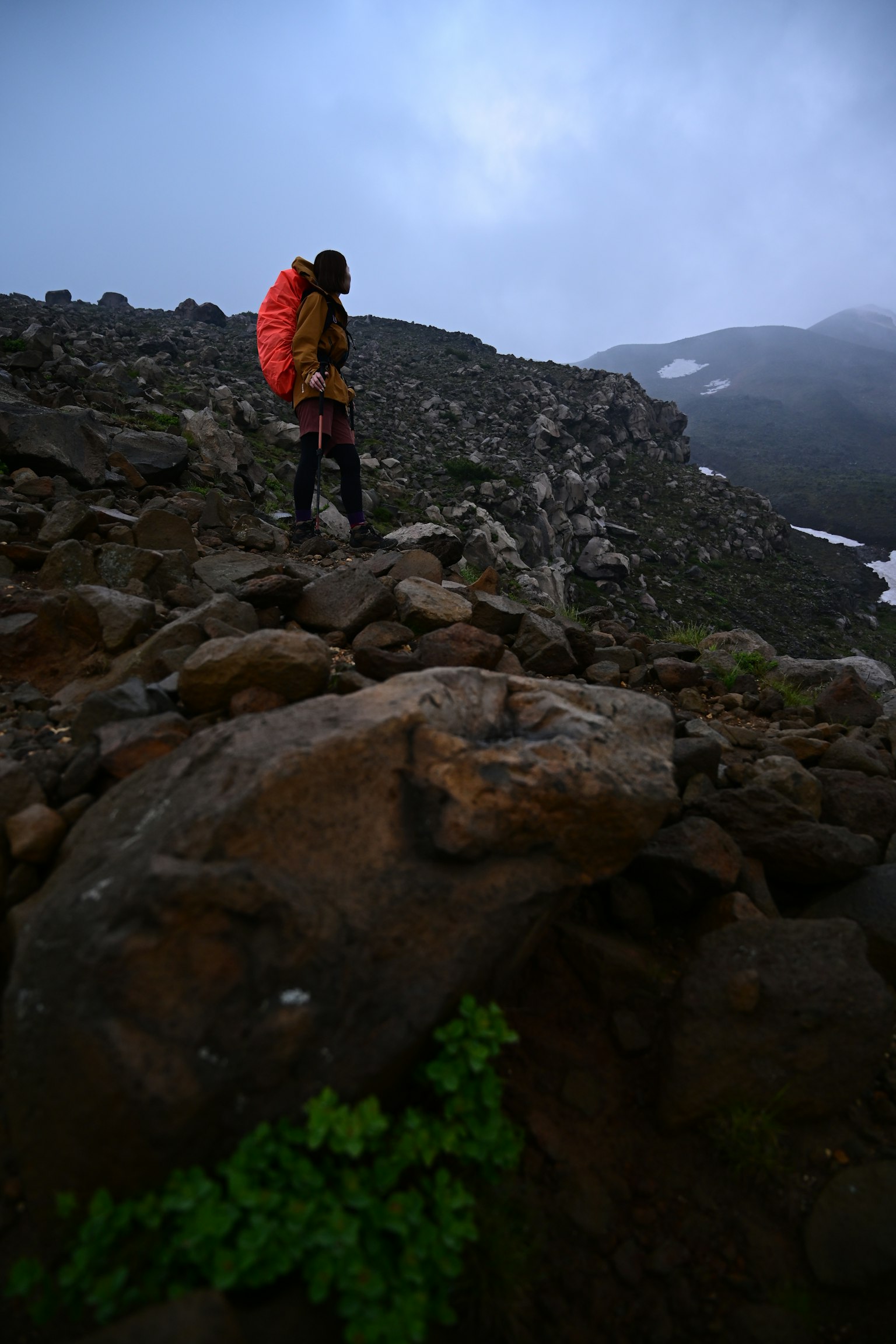 Wanderer steht auf Felsen mit einem orangefarbenen Rucksack in einer nebligen Berglandschaft