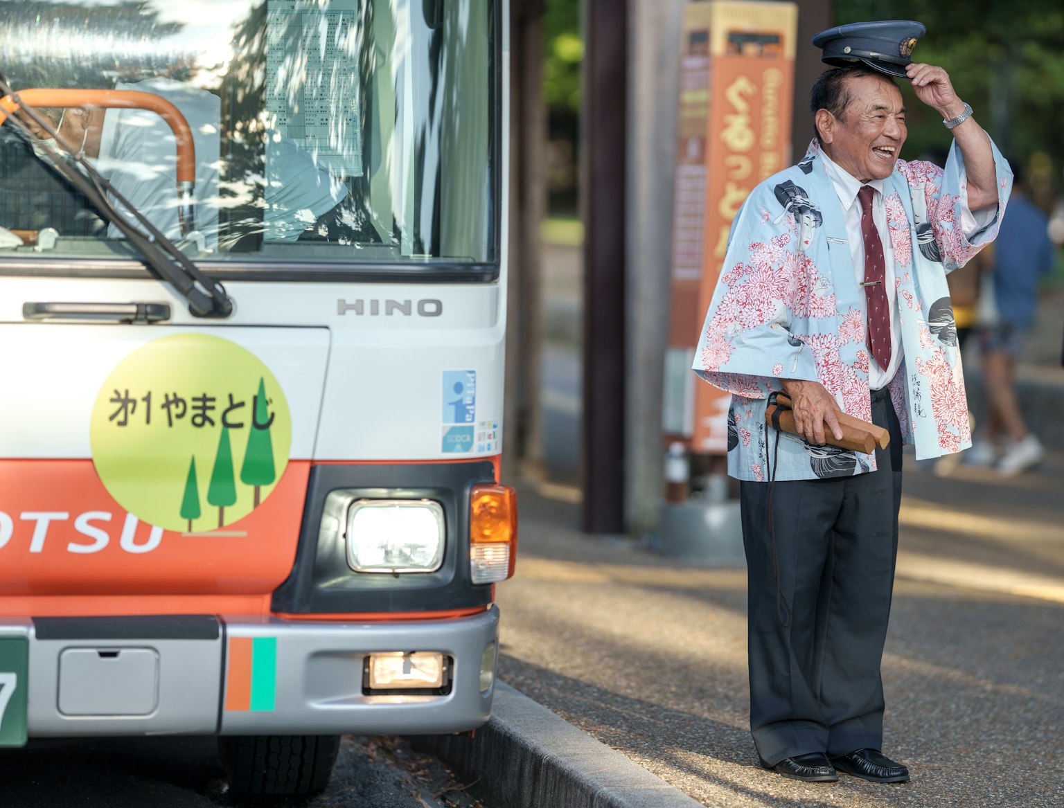 在公車站旁邊的公車旁邊拿著帽子的男人