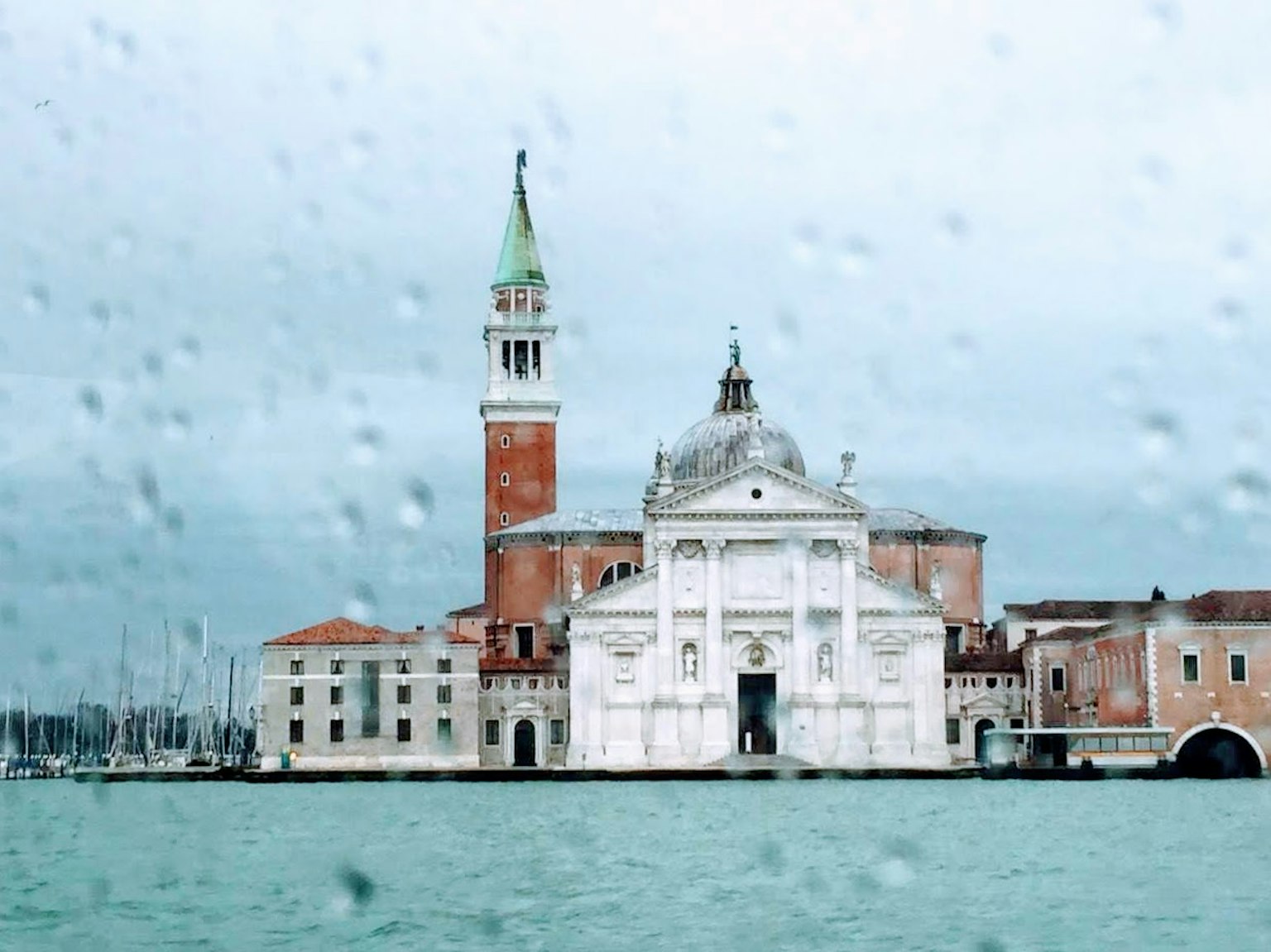 Blick auf ein weißes Gebäude und einen Glockenturm in Venedig durch Regentropfen auf einem Fenster