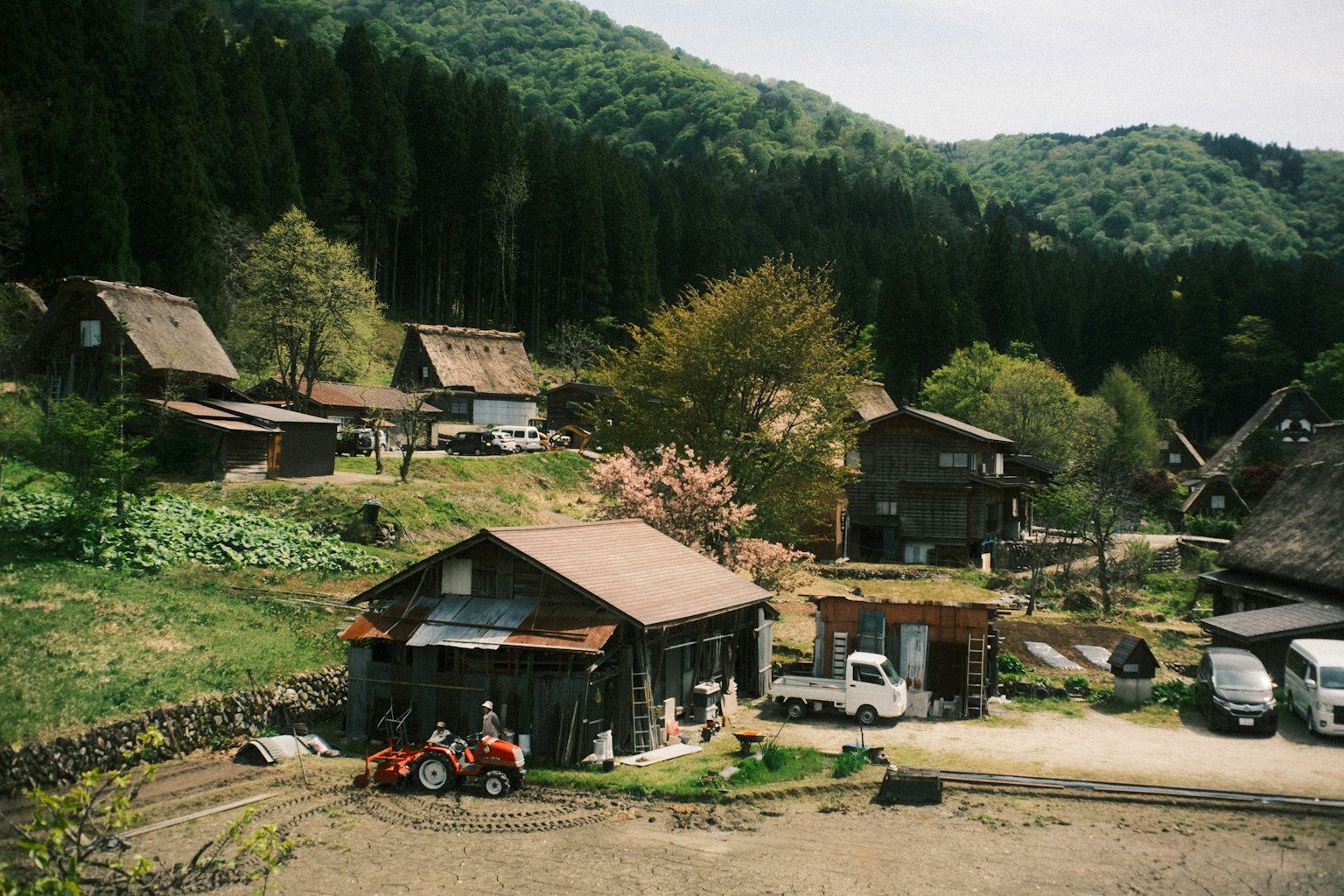 被郁郁蔥蔥的山脈環繞的傳統日本鄉村風景，古老的木屋和一輛拖拉機