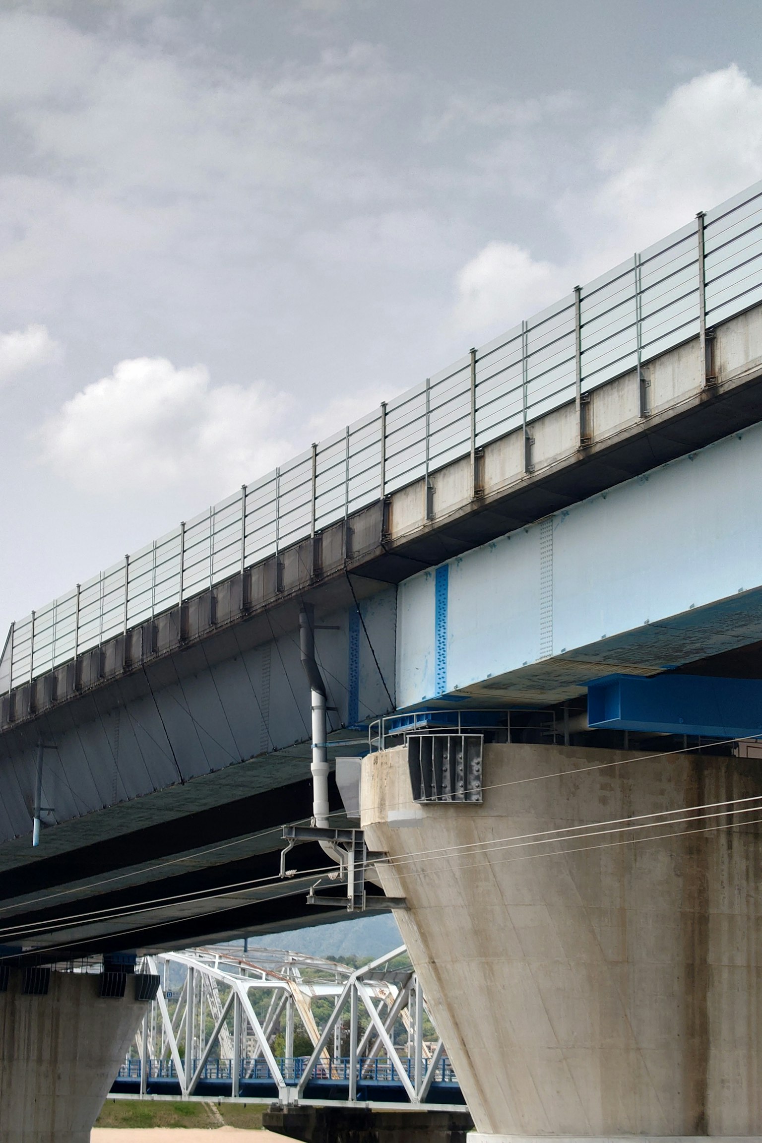 Vue d'un pont bleu avec des supports en béton et un ciel nuageux