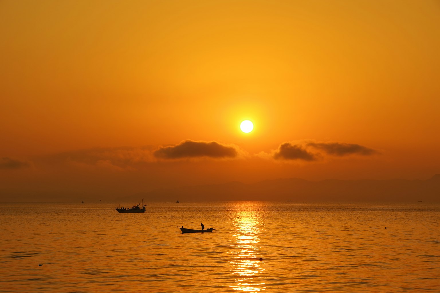 Coucher de soleil sur l'océan avec des bateaux silhouettés contre un ciel orange